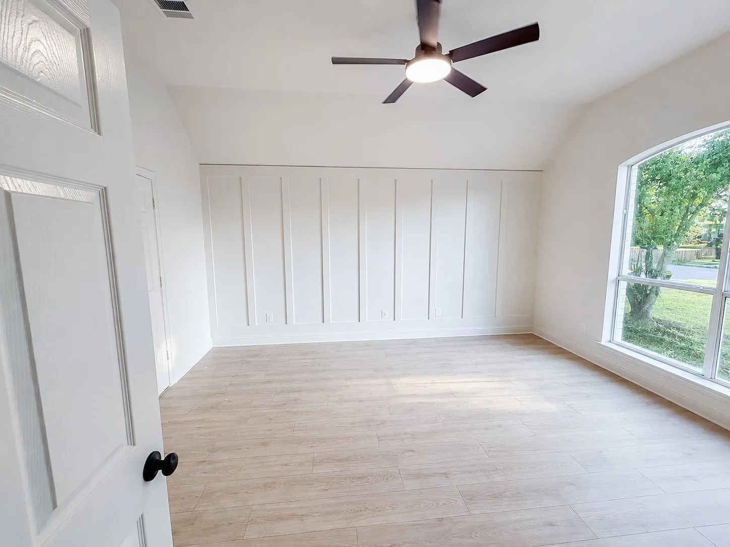 Bright, spacious primary bedroom with vaulted ceilings, modern ceiling fan, large picture window, and designer accent wall.