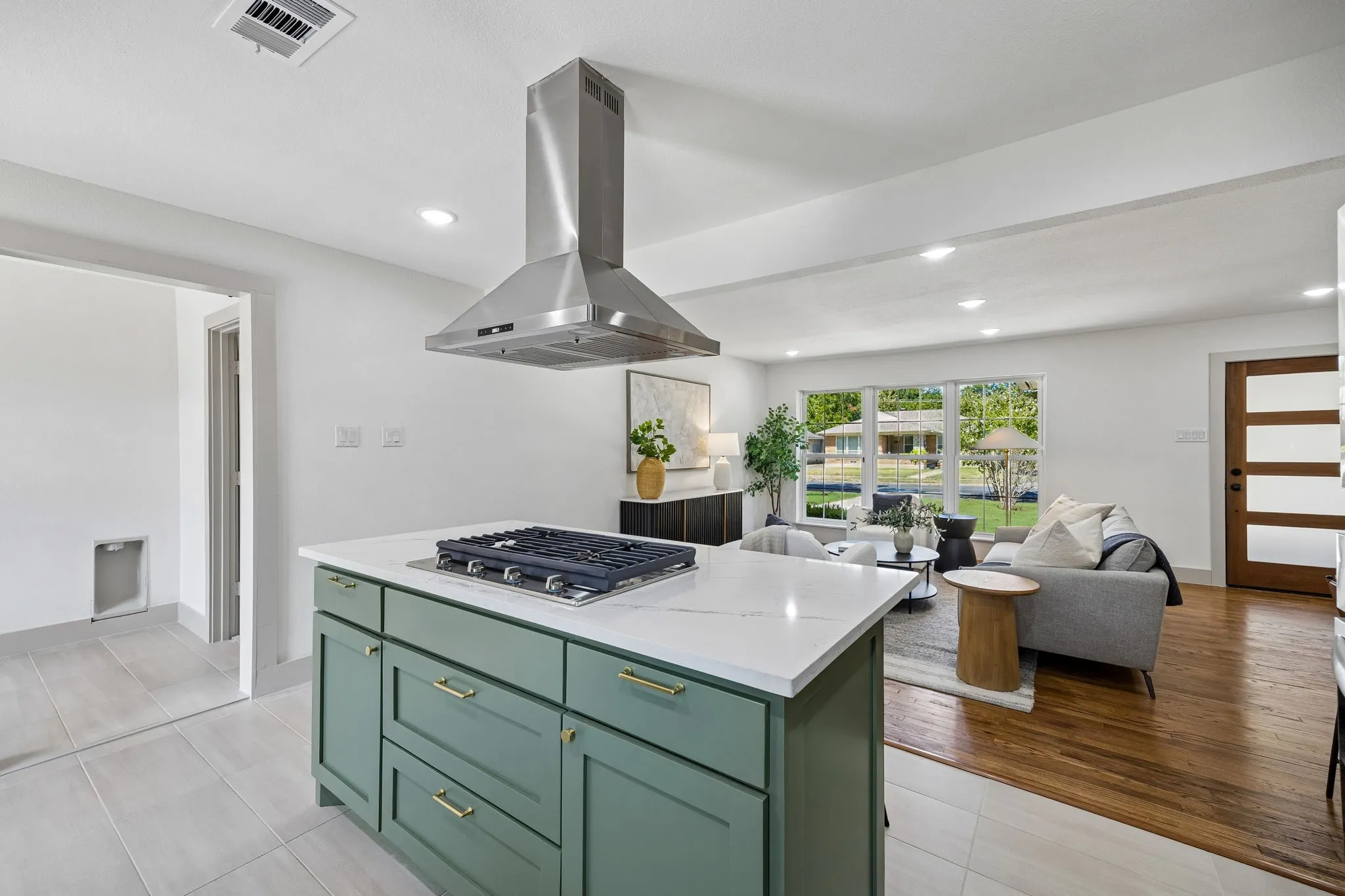 Kitchen island with a built-in cooktop, stainless steel range hood, white countertop, and green cabinetry with brass hardware