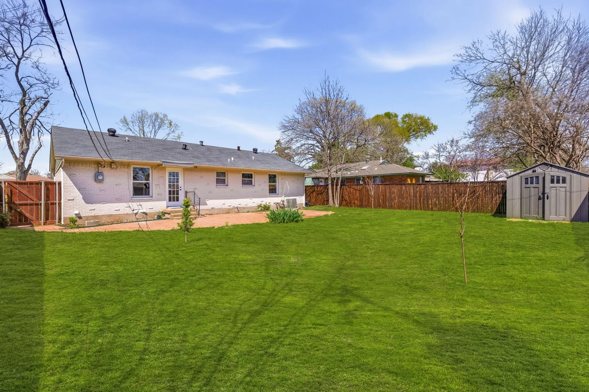Expansive lawn, brick exterior, full privacy fencing, exterior storage shed, and patio area