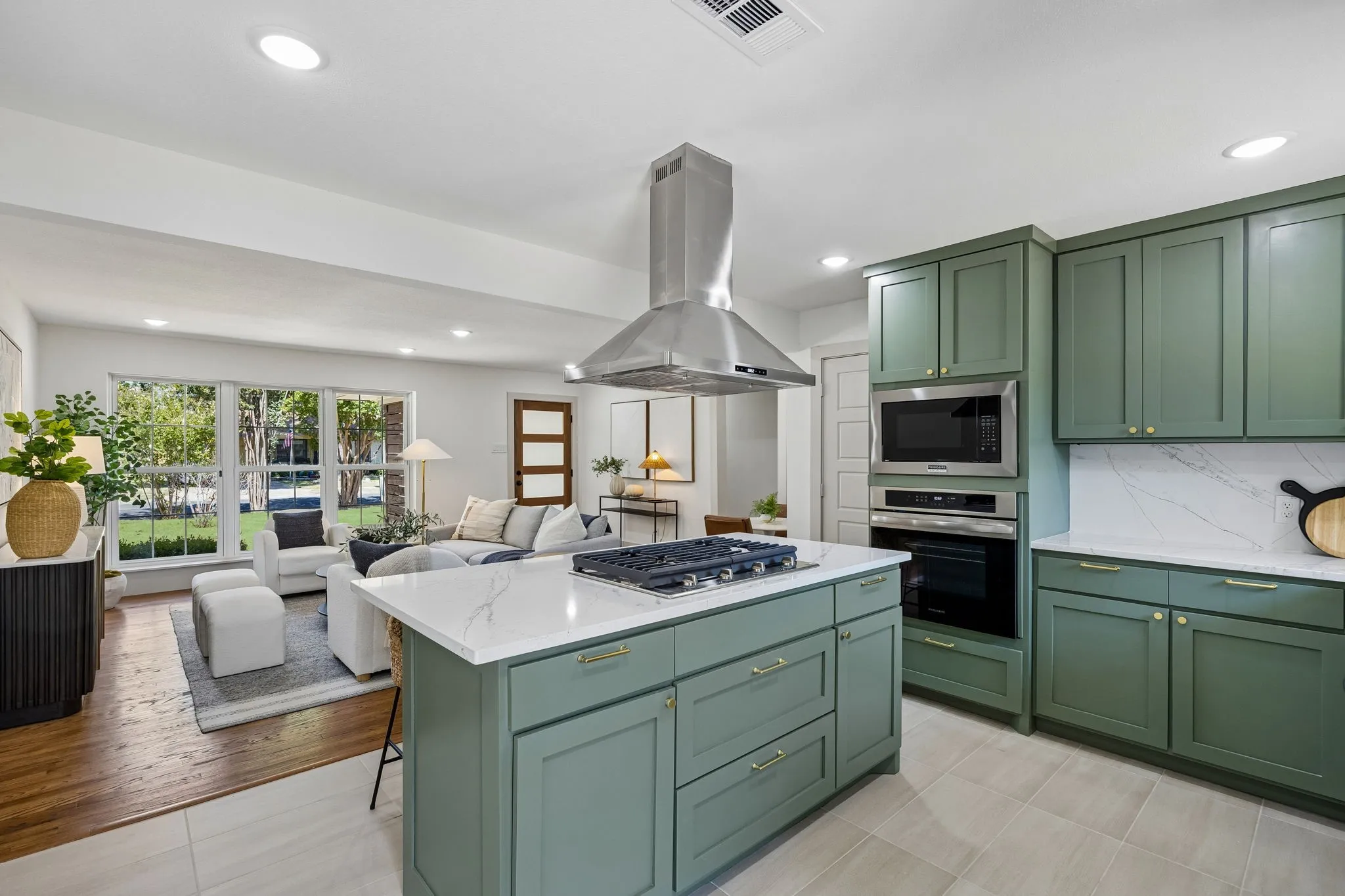 Kitchen island with a built-in gas cooktop, stainless steel range hood, integrated microwave and oven, green cabinetry, and white countertops