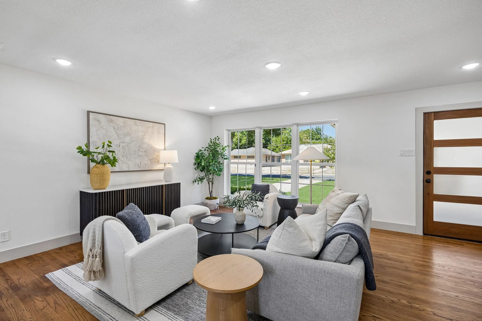 Recessed lighting throughout, wood-finish flooring, white painted walls, large window with outdoor visibility, and a wood-panel door with translucent inserts