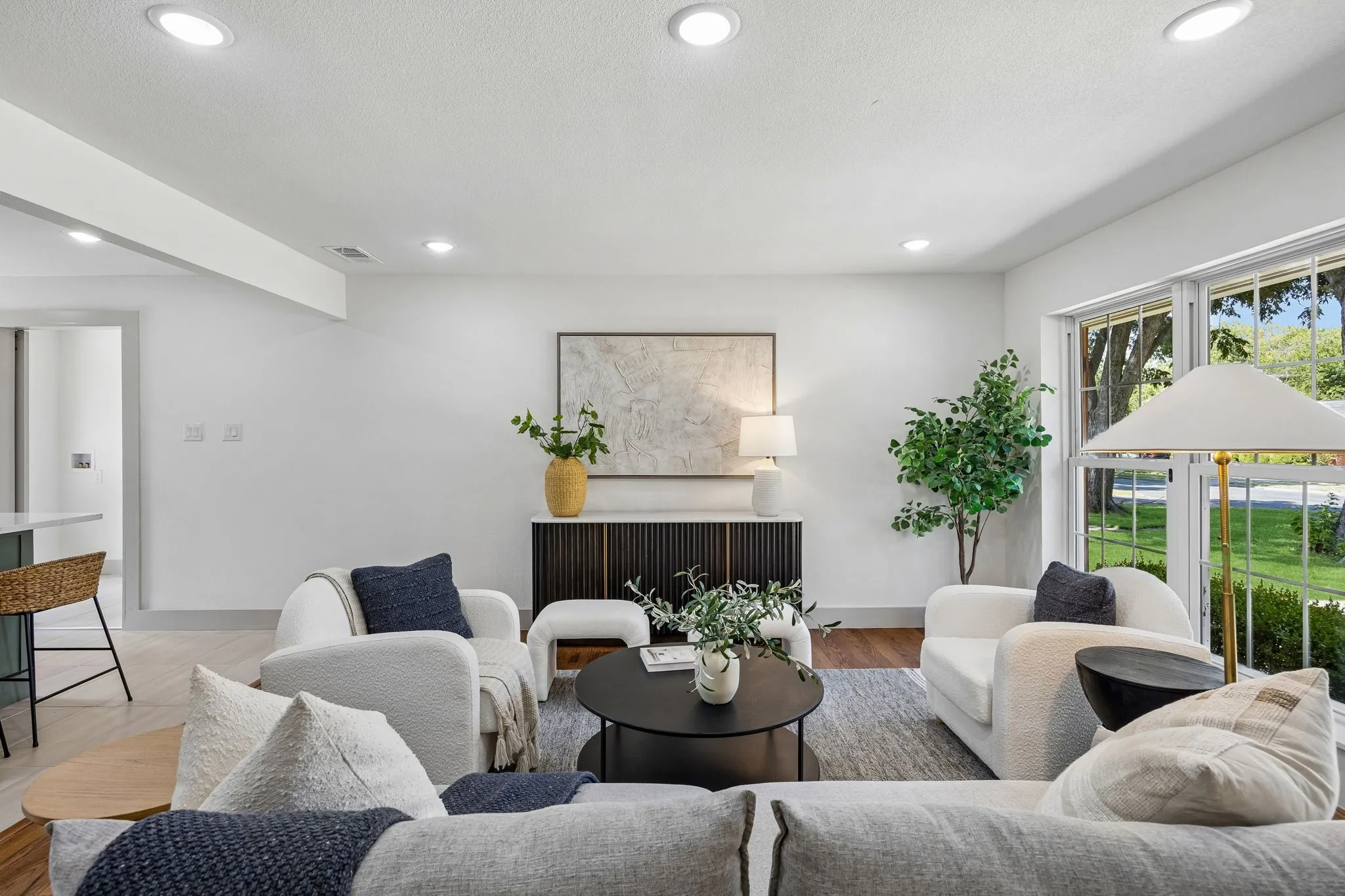 Recessed lighting throughout, wide plank wood-finish flooring, white walls, and large windows with exterior foliage
