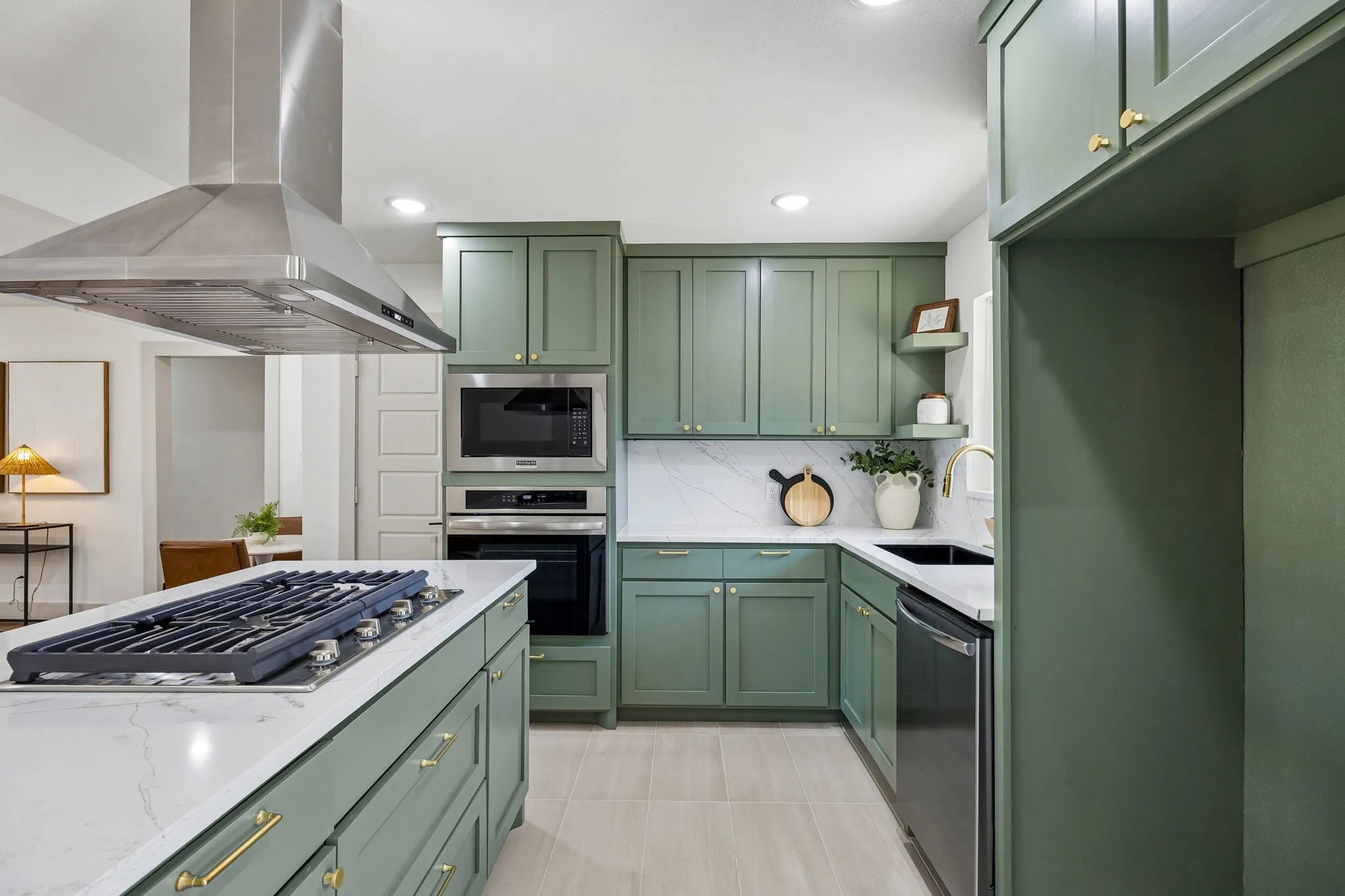 Kitchen featuring sage green cabinetry, quartz countertops, stainless steel appliances, a center island with a cooktop, and a stainless steel range hood
