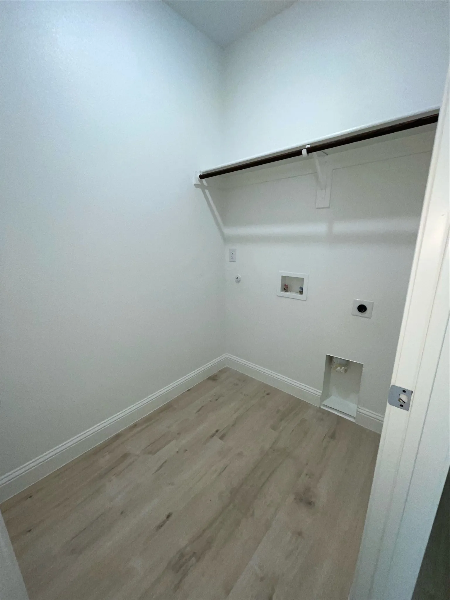 Dedicated laundry area featuring a built-in shelf, hanging rod, wood-finish flooring, and white walls