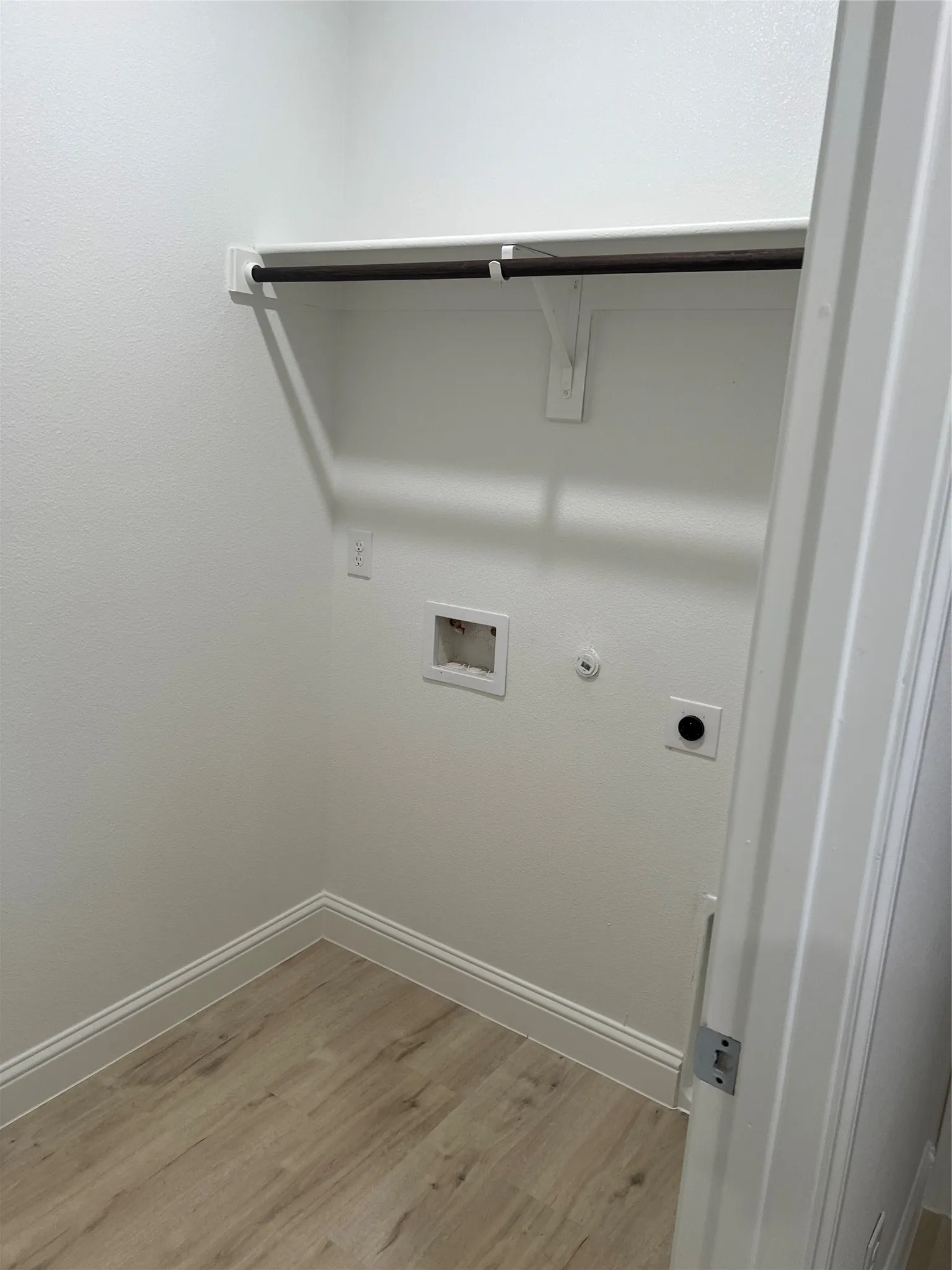 Utility space featuring a wood-finish flooring, white walls, and a built-in hanging rod
