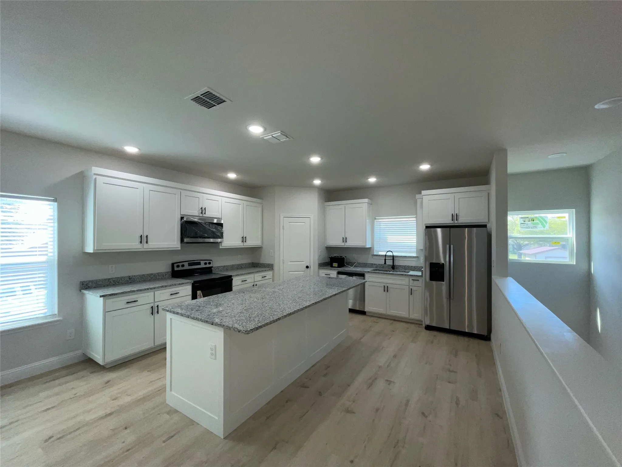 Kitchen featuring white shaker cabinetry, granite countertops, an island, recessed lighting, and wood-finish flooring