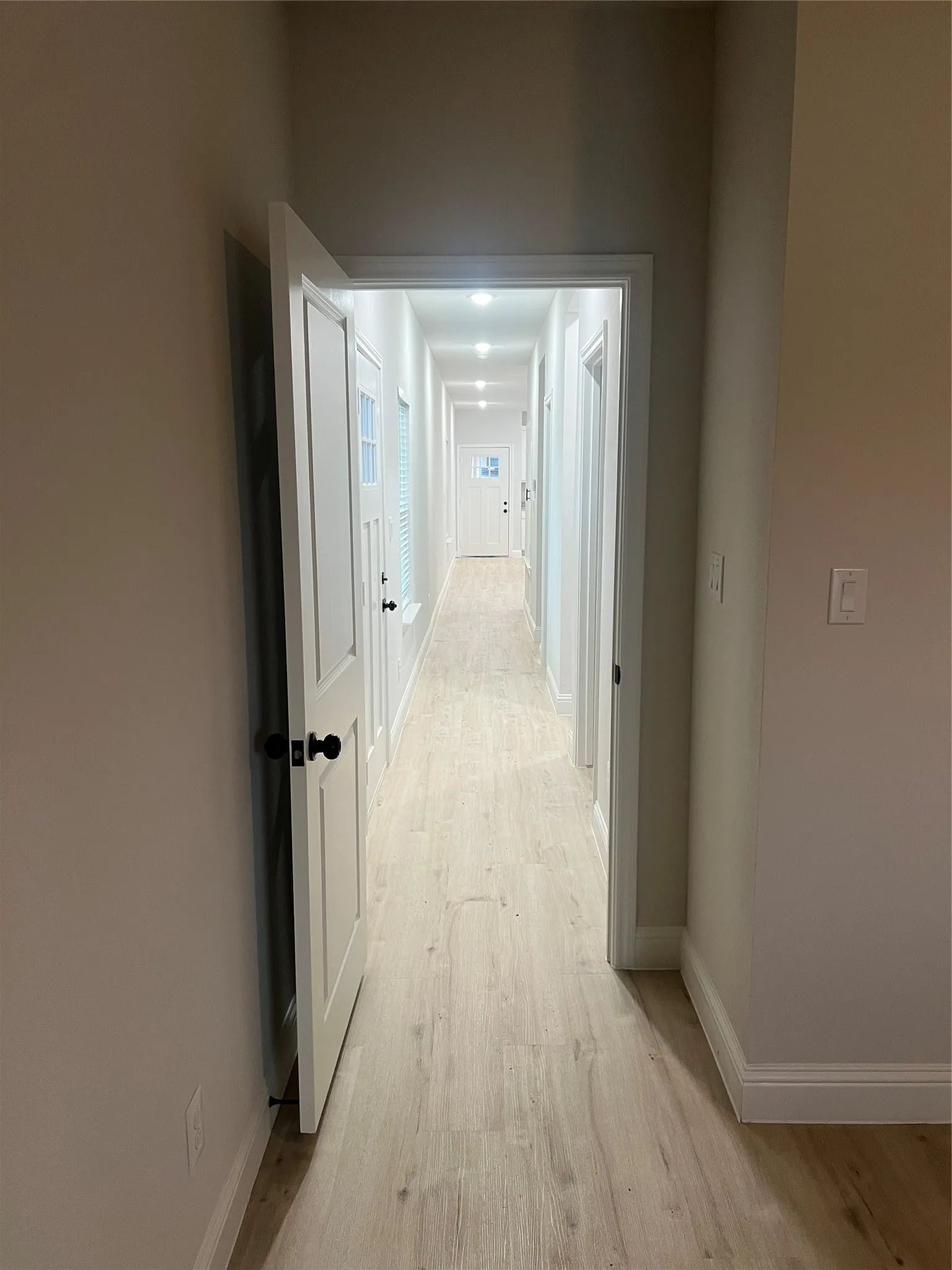 Hallway featuring wood-finish flooring, recessed lighting, and white paneled doors with matte black hardware