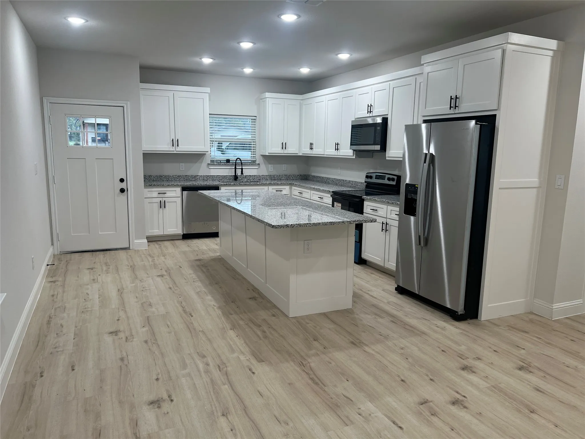 Kitchen with light wood-finish flooring, white cabinetry, granite countertops, and stainless steel appliances