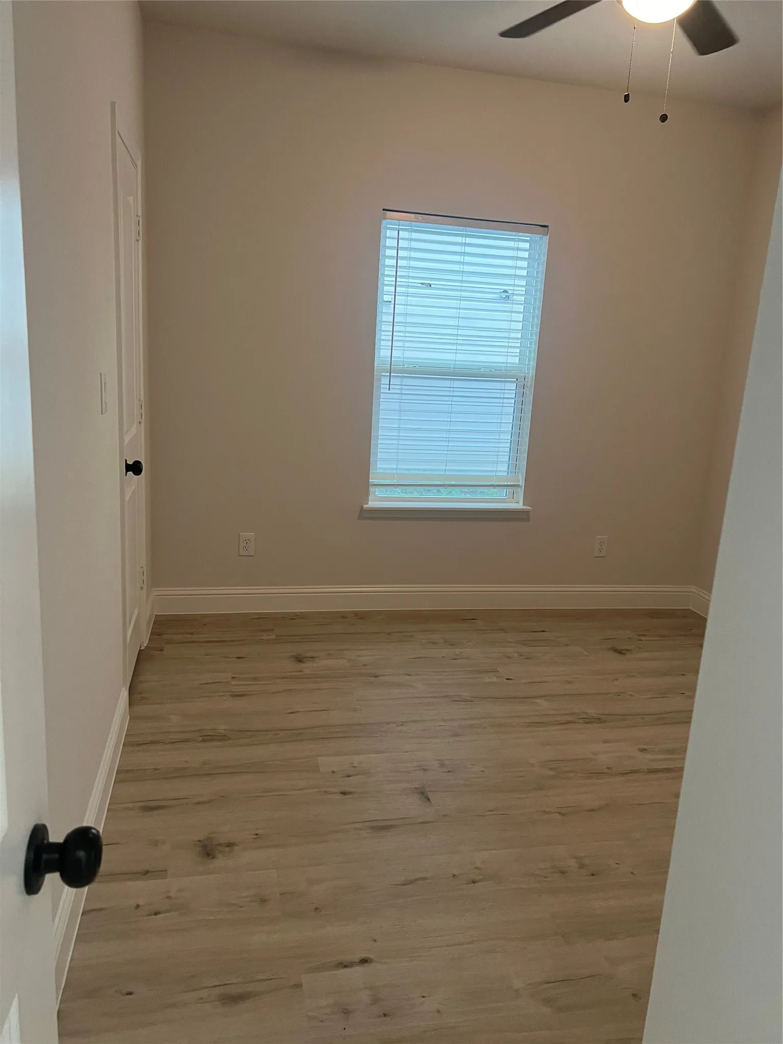 Vaulted ceiling with a ceiling fan, window with blinds, wood-finish flooring, and a paneled door with a black doorknob