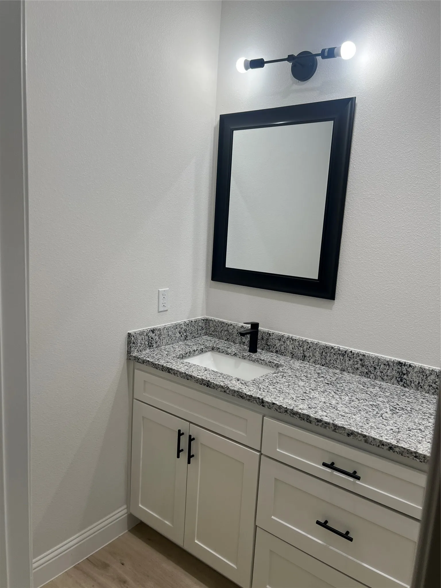 White shaker-style vanity with matte black hardware, granite countertop, undermount sink, and matte black faucet