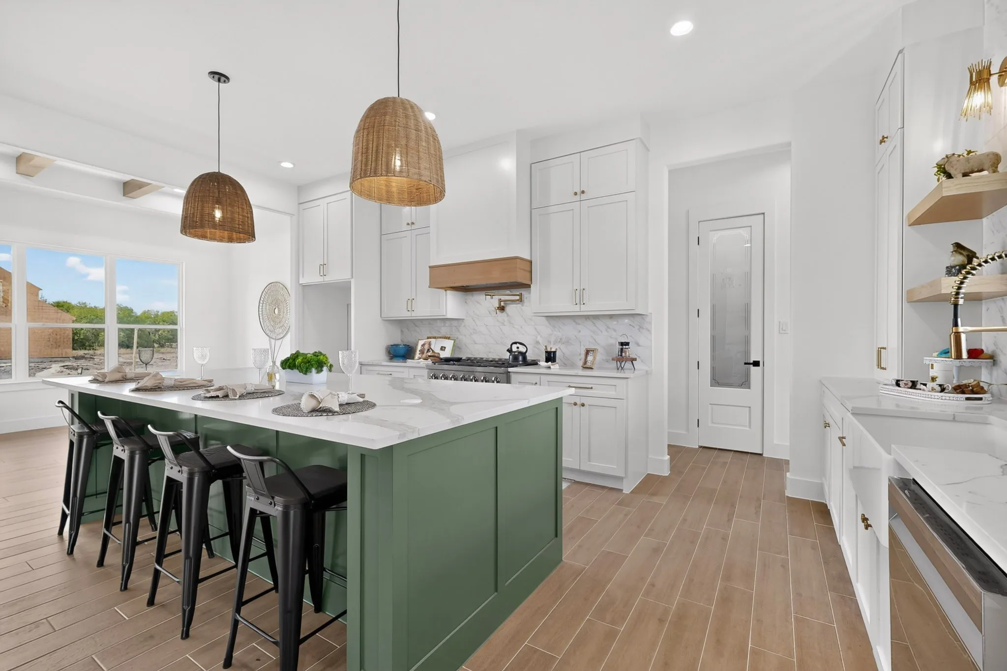 Expansive kitchen featuring a large island with seating, white shaker cabinetry, stainless steel range, wood-finish flooring, and a glass-paneled pantry door