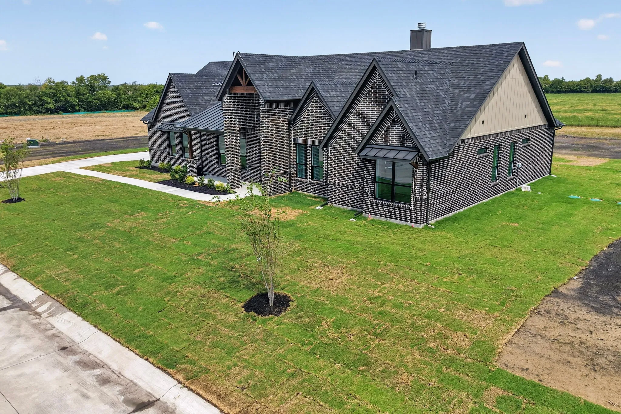 Brick facade, dark shingle roof, gabled architectural elements, multiple windows, and a paved walkway