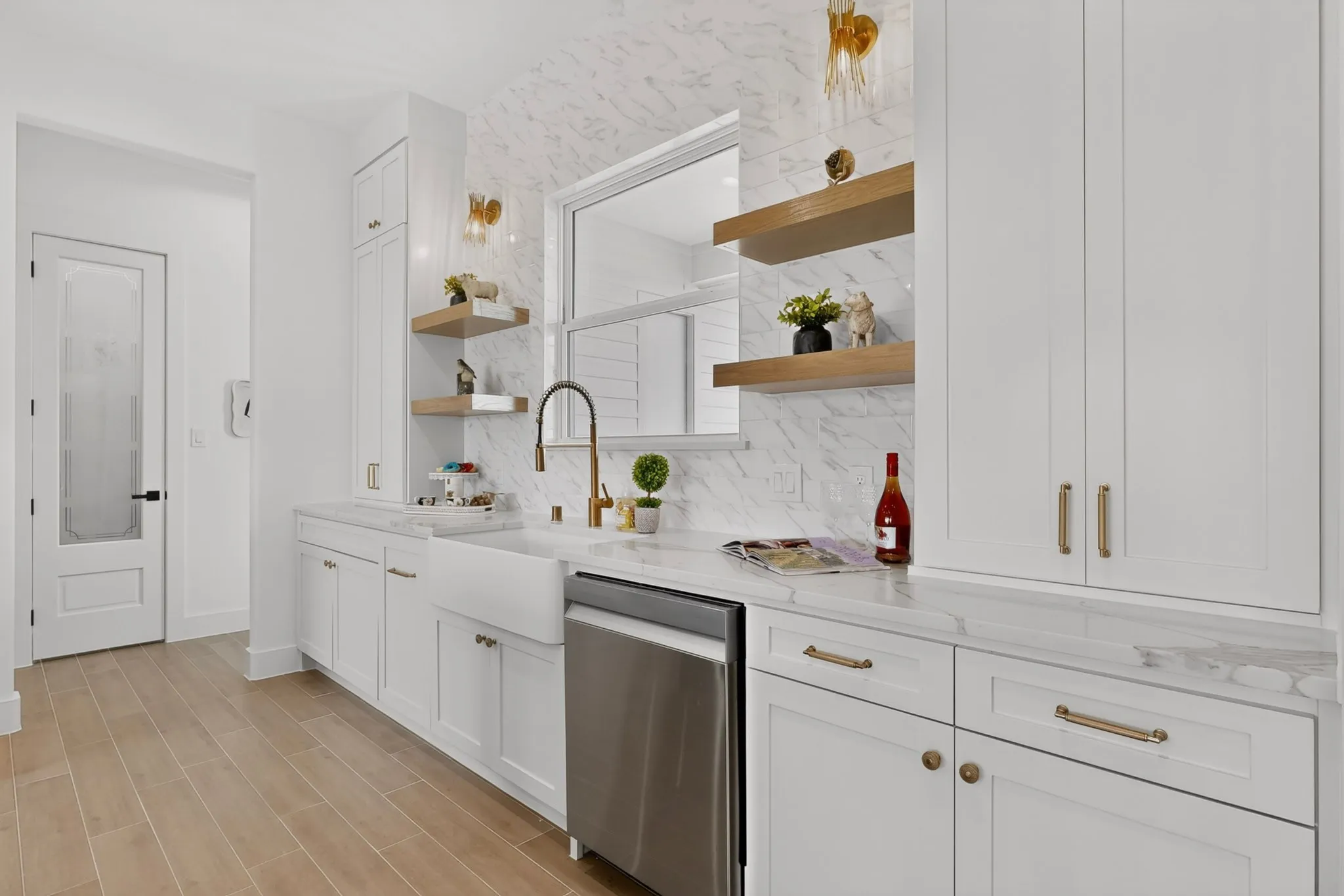 White shaker cabinetry with gold-tone hardware, farmhouse sink, wood-finish flooring, white marble-look countertops, and a white marble-look backsplash