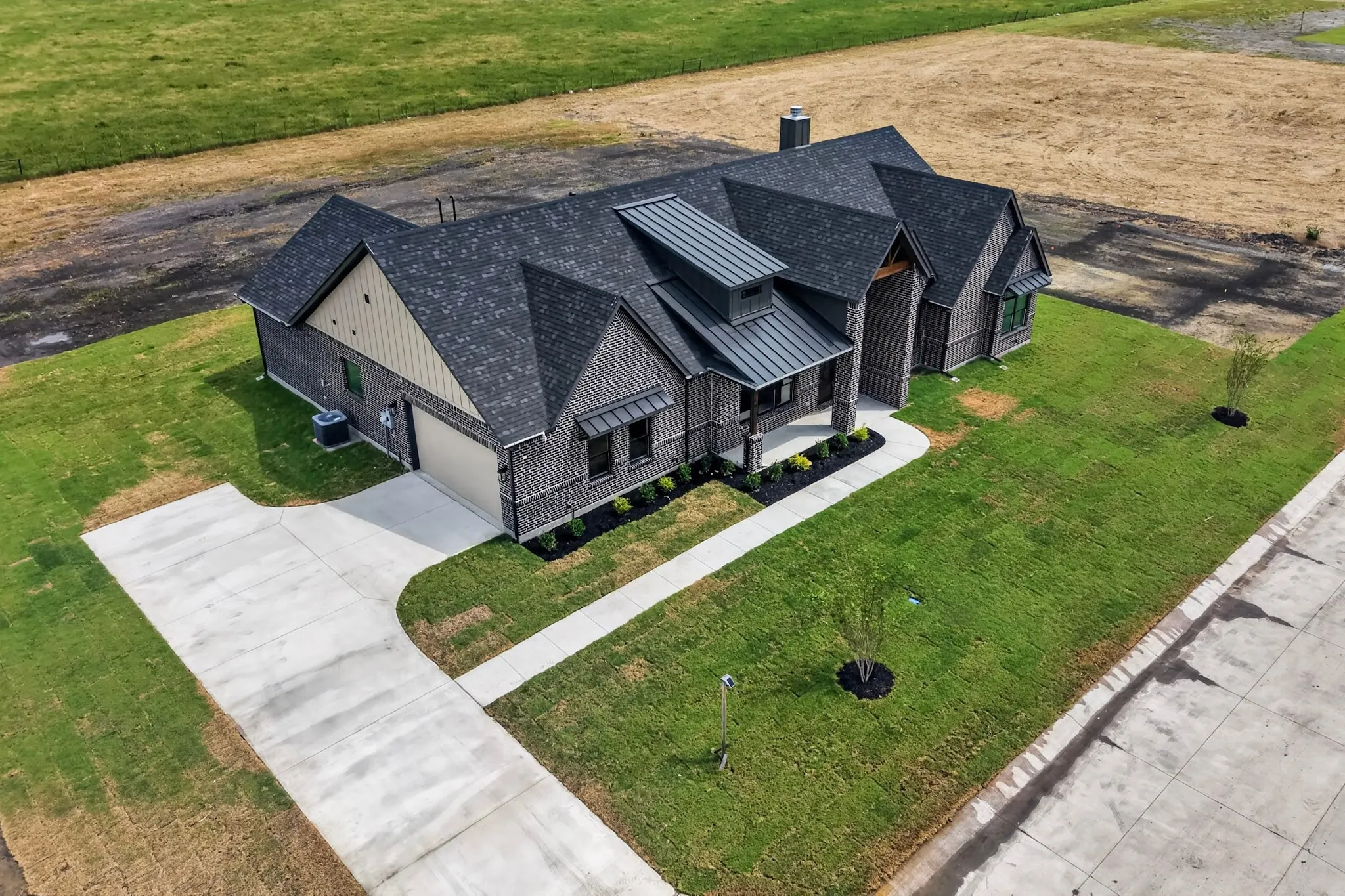 Brick exterior with a prominent front entrance, multiple roof planes, a two-car garage, an expansive concrete driveway, and a manicured lawn