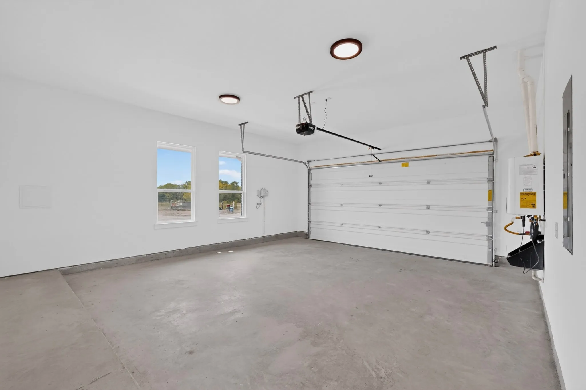 Concrete flooring, two windows, two ceiling-mounted light fixtures, garage door, and a wall-mounted water heater