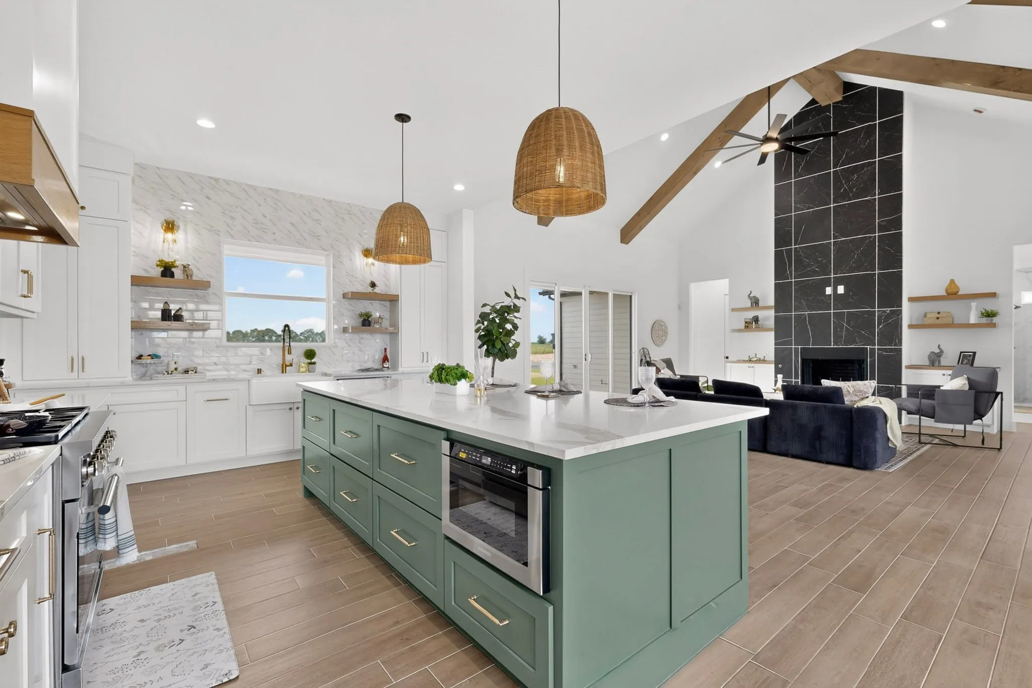 Expansive kitchen island with built-in microwave, white shaker cabinetry, wood-finish flooring, vaulted ceilings with exposed beams, and a floor-to-ceiling fireplace with dark tile surround