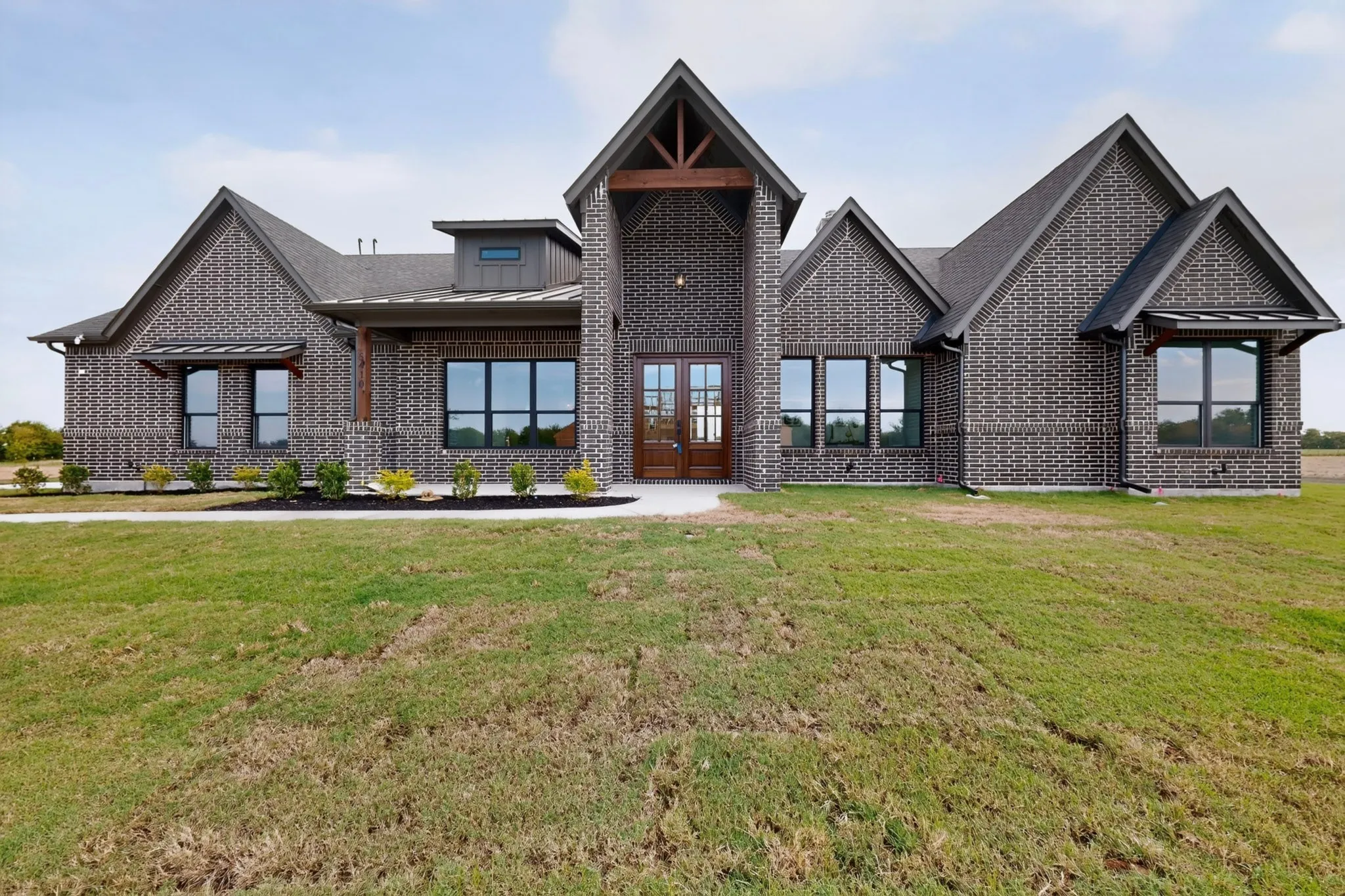 Brick exterior with dark gray tones, prominent gables, large multi-pane windows, and a double-door entry