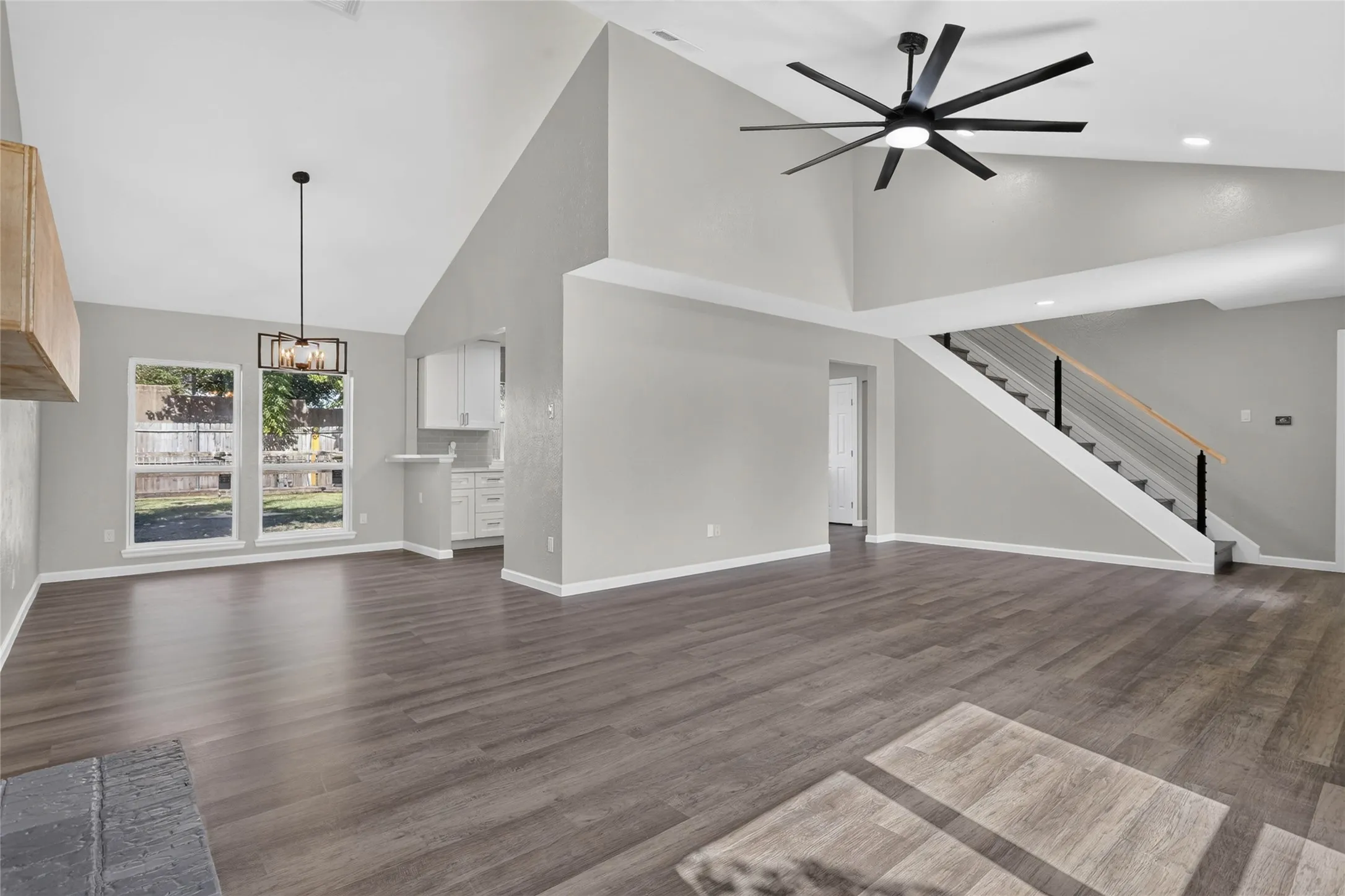 Vaulted ceilings, wood-finish flooring, contemporary ceiling fan, modern staircase with metal balusters, and a built-in kitchen pass-through