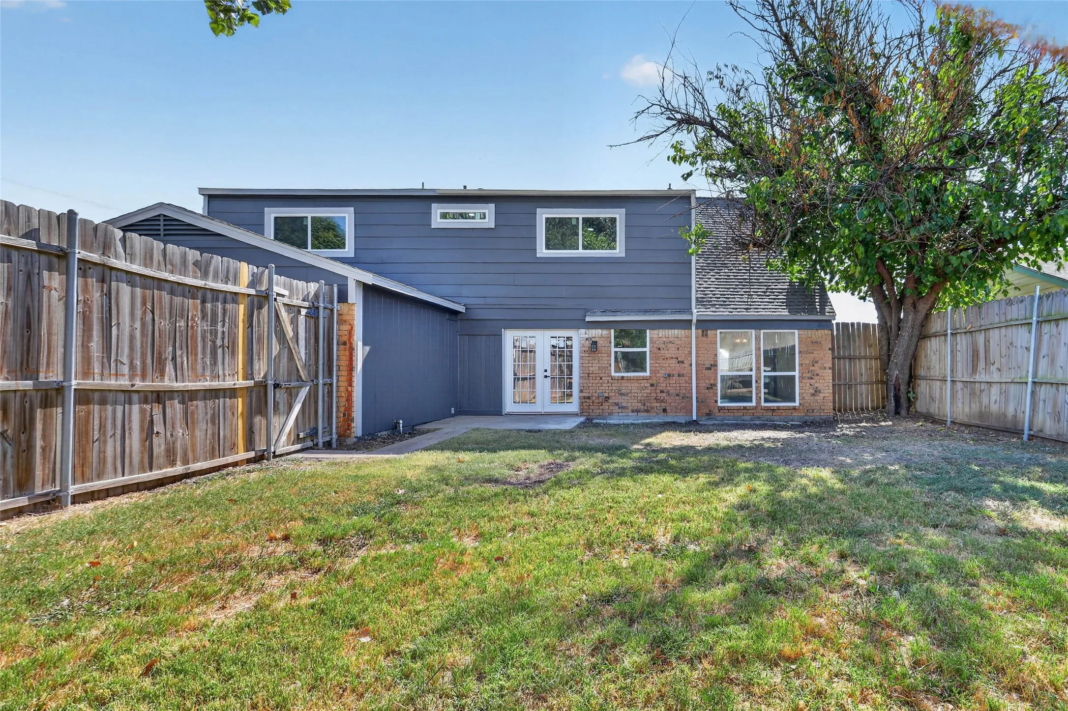 Fenced backyard featuring a patio, brick and siding exterior, and mature trees