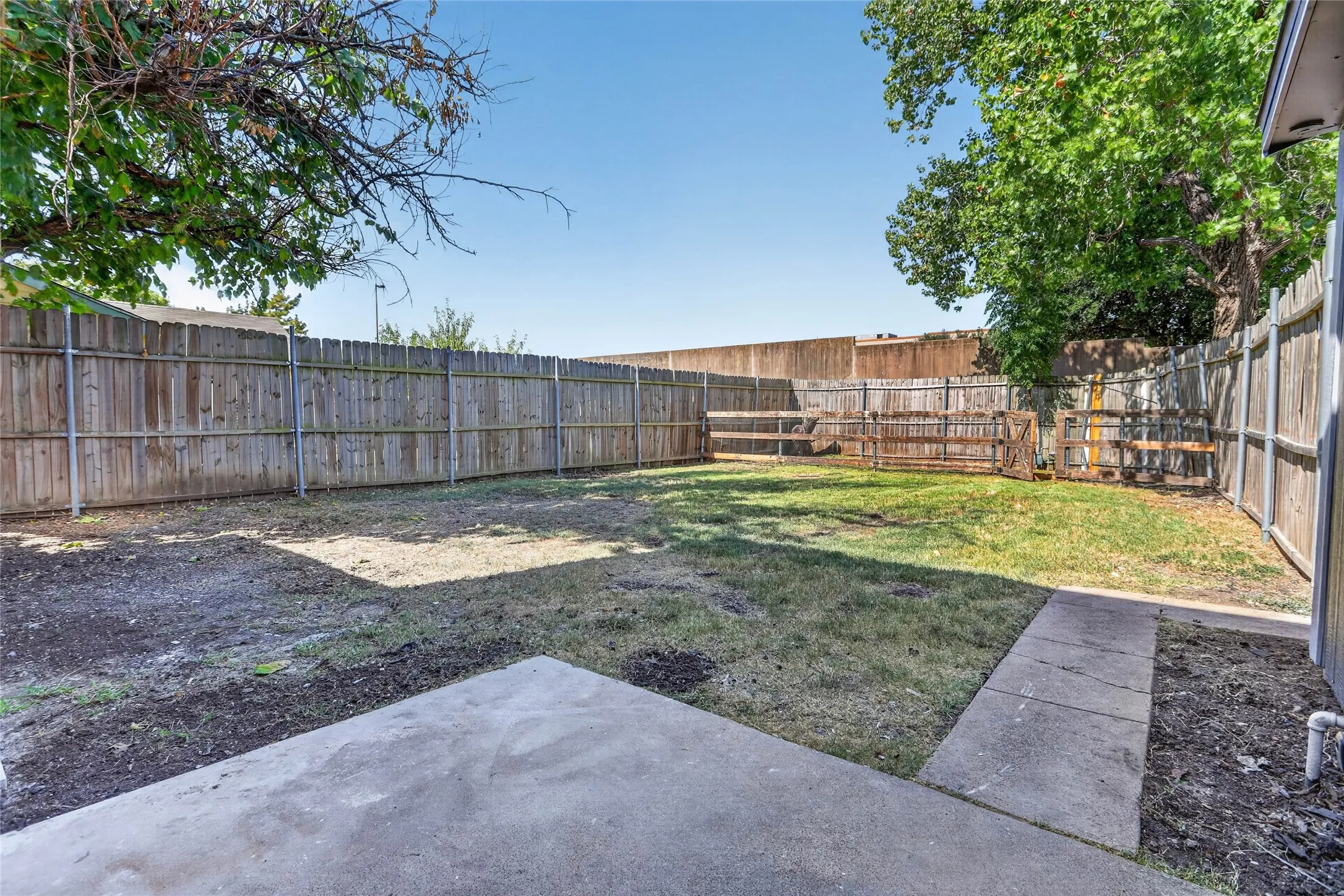 Enclosed backyard featuring a concrete patio, wood fencing, and mature trees