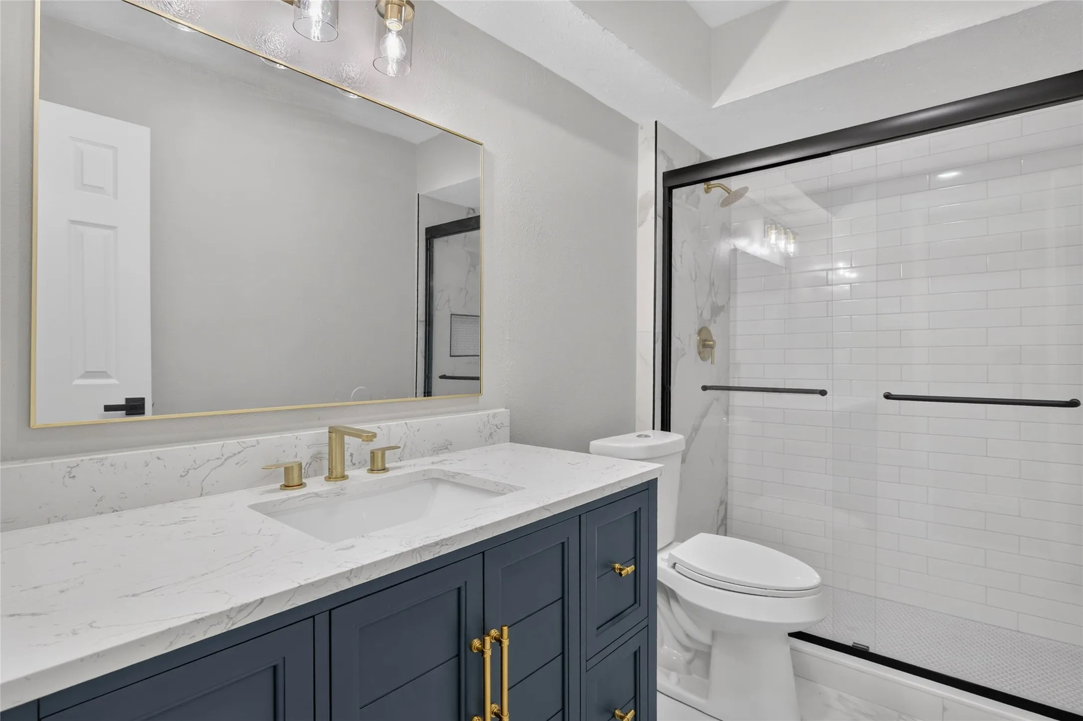 Vanity with a quartz countertop, gold-tone fixtures, and a large framed mirror