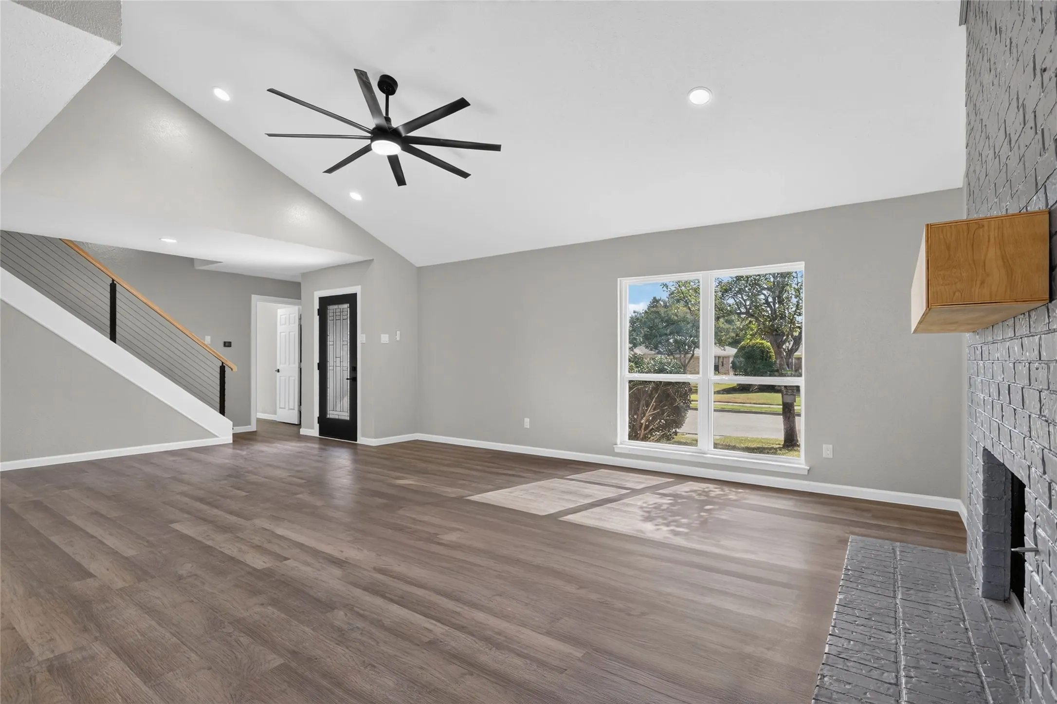 Vaulted ceiling with recessed lighting and ceiling fan, wood-finish flooring, painted brick fireplace with wood mantel, and large picture window