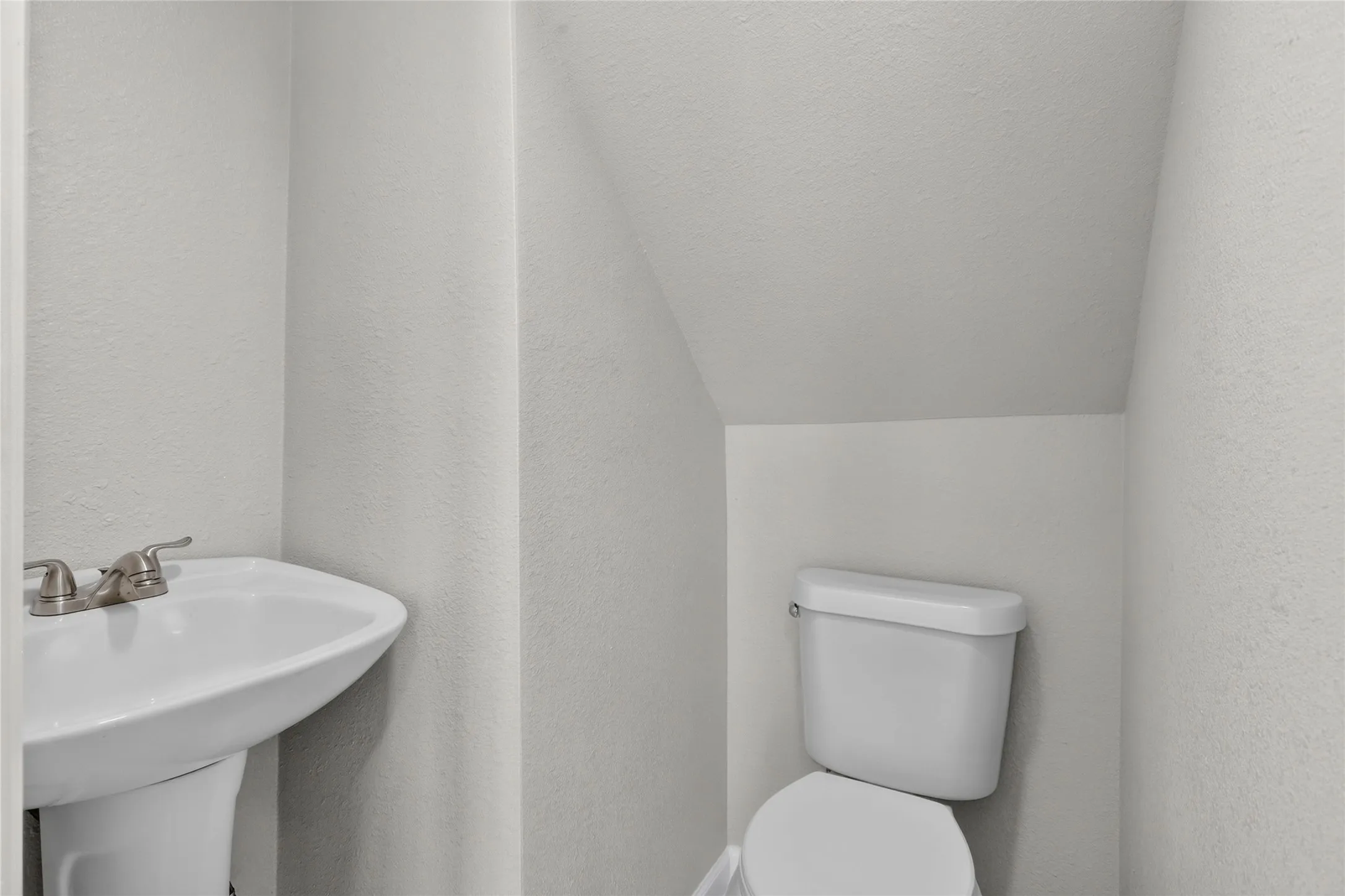 Pedestal sink with brushed nickel faucet, white toilet, and textured walls