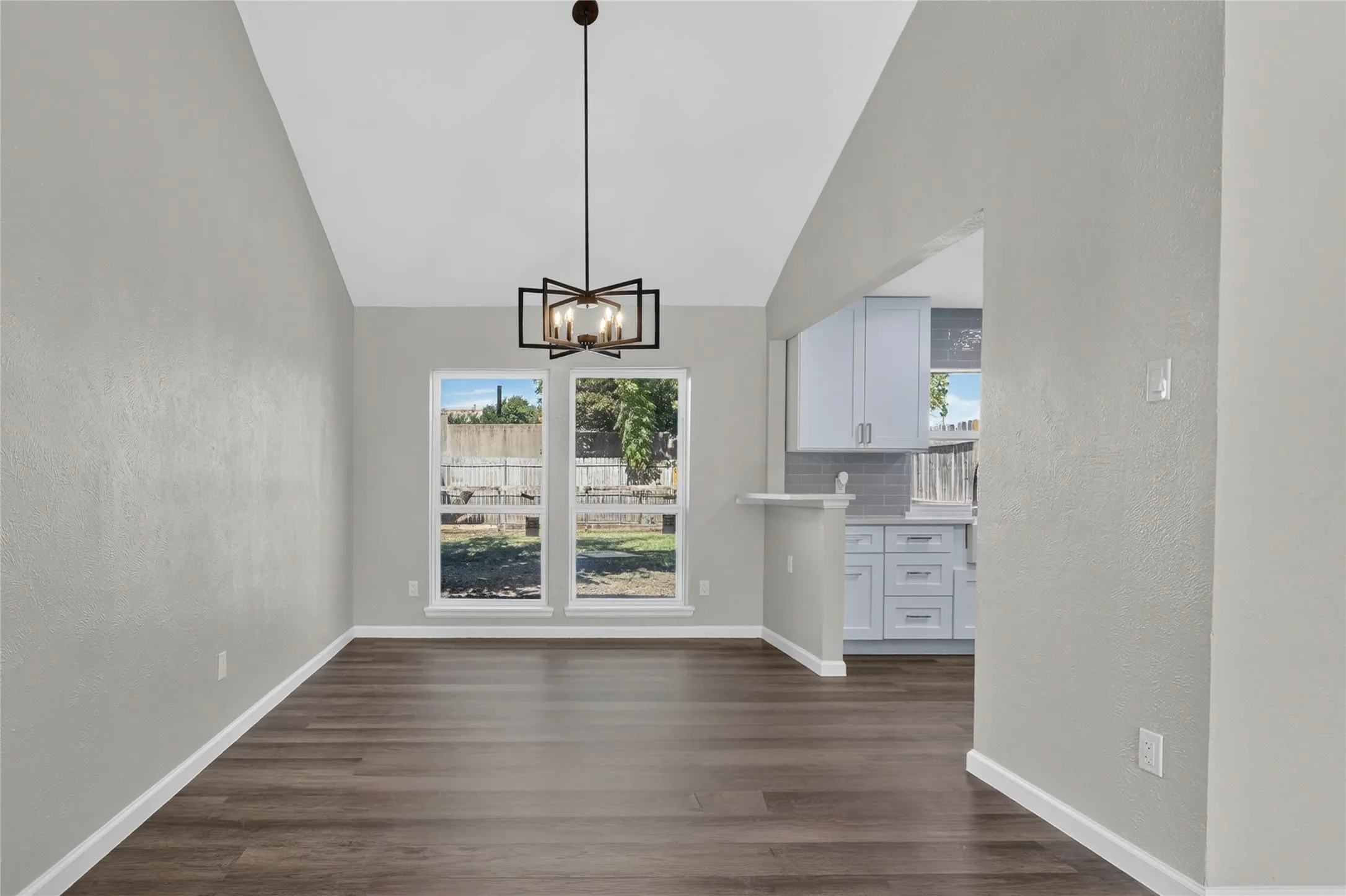 Vaulted ceiling with a geometric chandelier, wood-finish flooring, and multiple windows