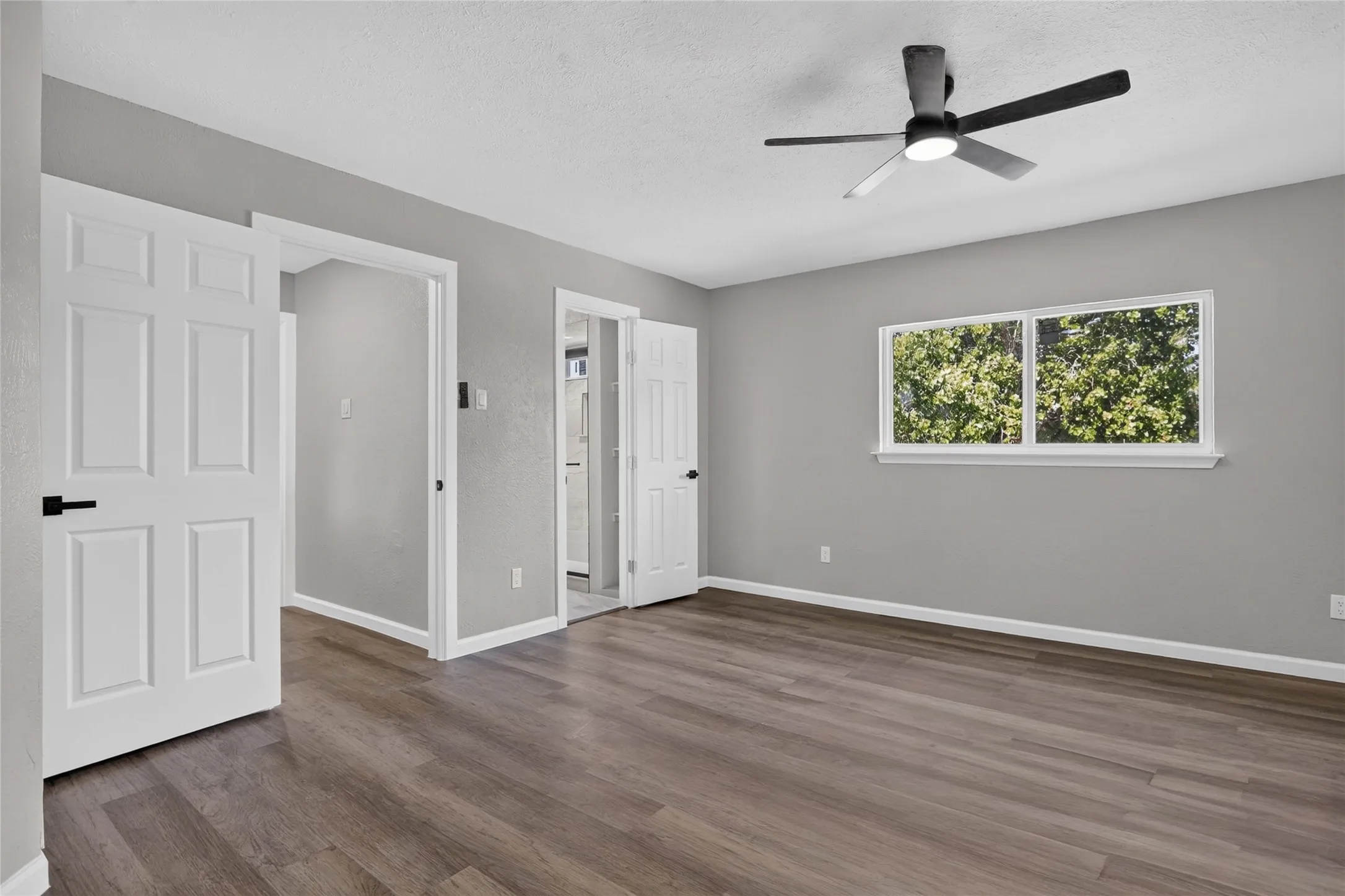 Wood-finish flooring, light grey wall paint, white trim, modern ceiling fan, and white paneled doors