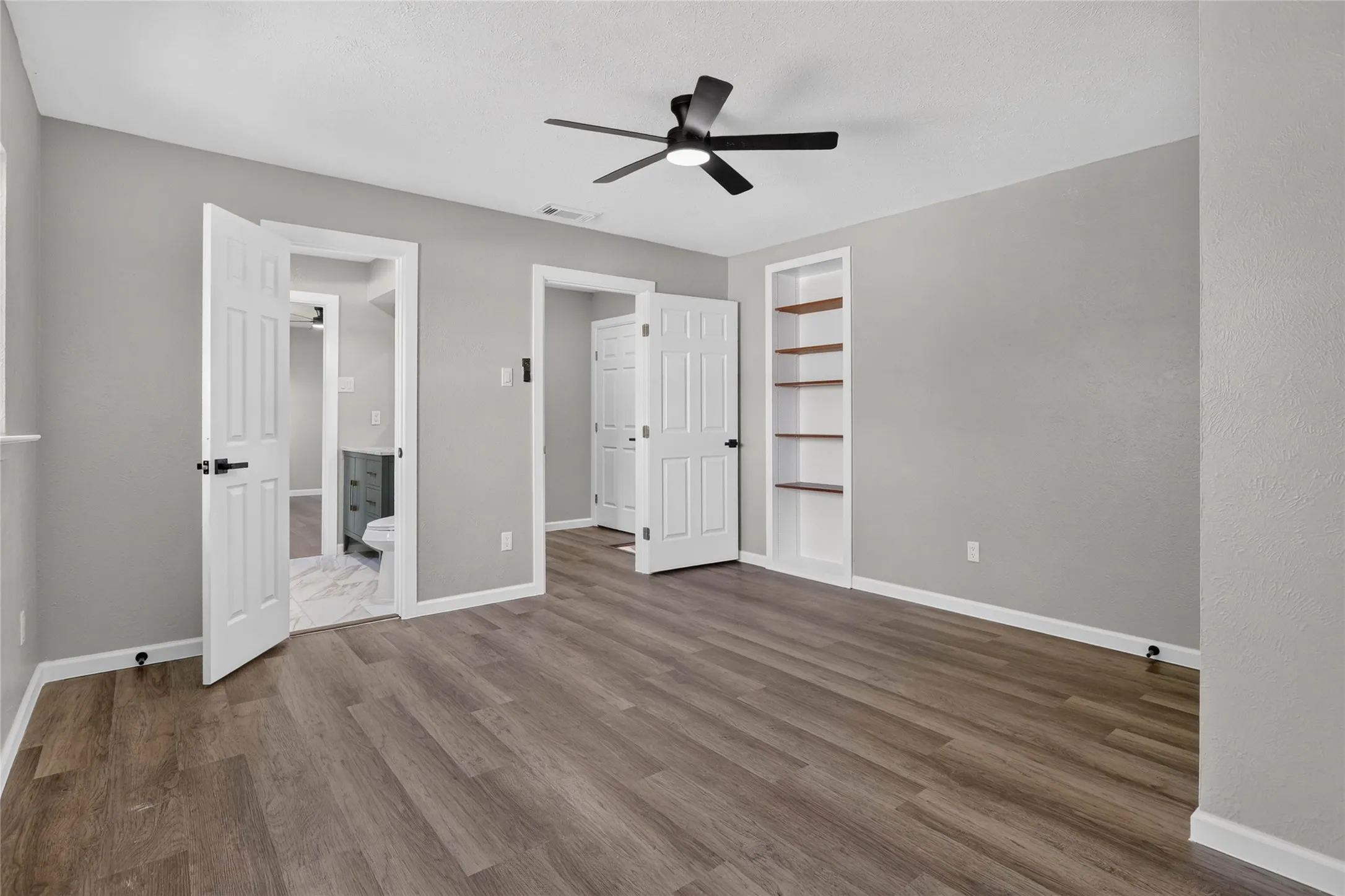 Wood-finish flooring with light gray walls, built-in shelving, and a ceiling fan