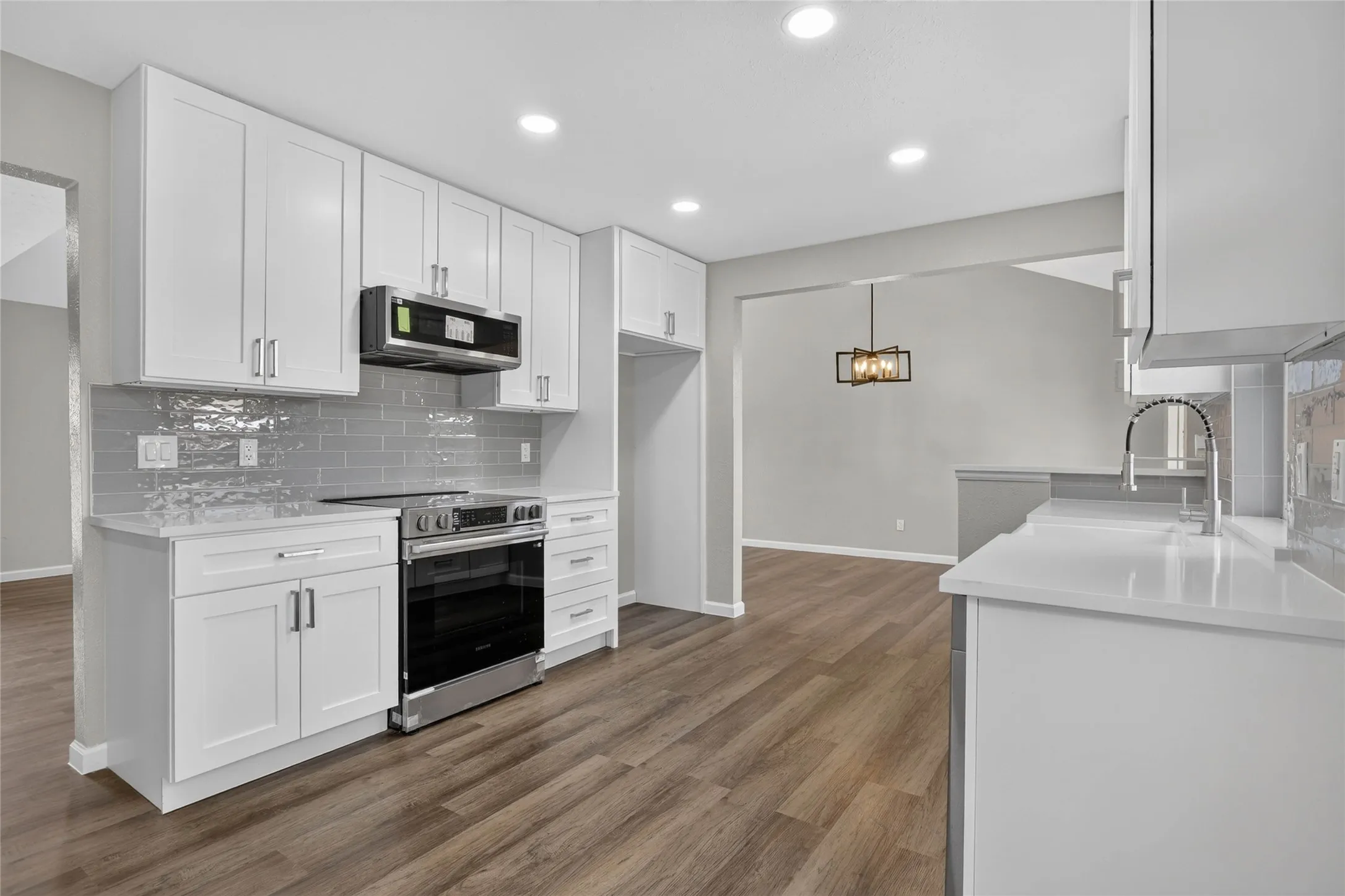 White shaker cabinetry, quartz countertops, stainless steel appliances, grey subway tile backsplash, and wood-finish flooring