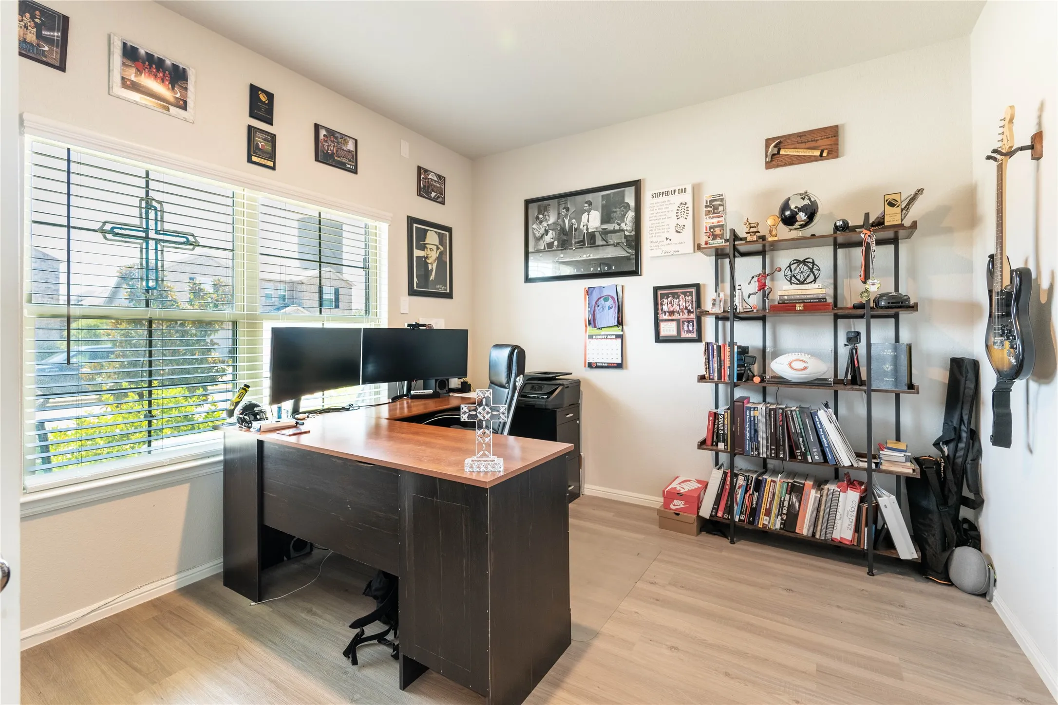 Light wood-finish flooring, two large windows with horizontal blinds, and a built-in shelving unit with dark metal framing and wood shelves
