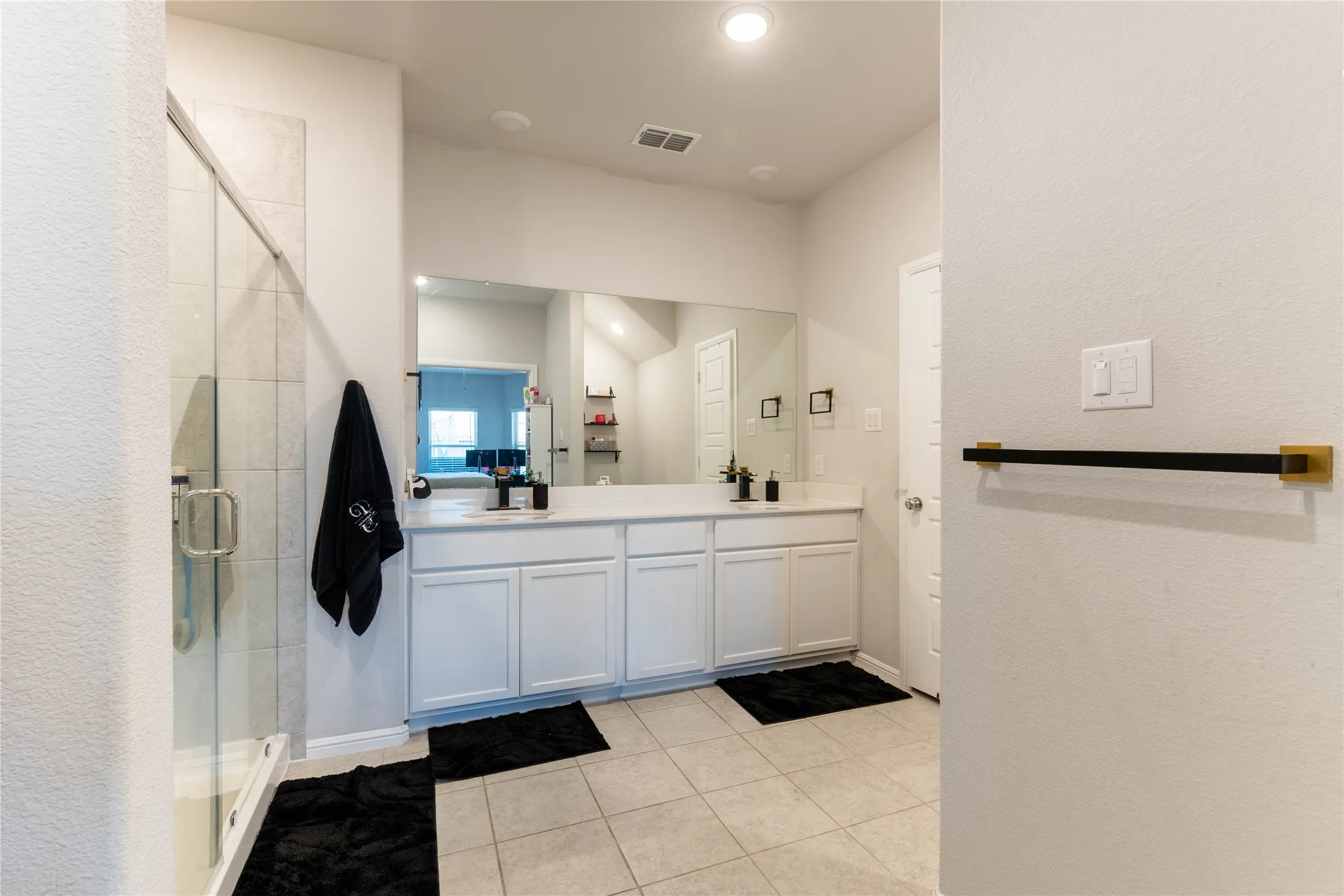 Dual vanity with white cabinetry and integrated sinks, large mirrored wall, glass-enclosed shower with tiled surround, and recessed lighting