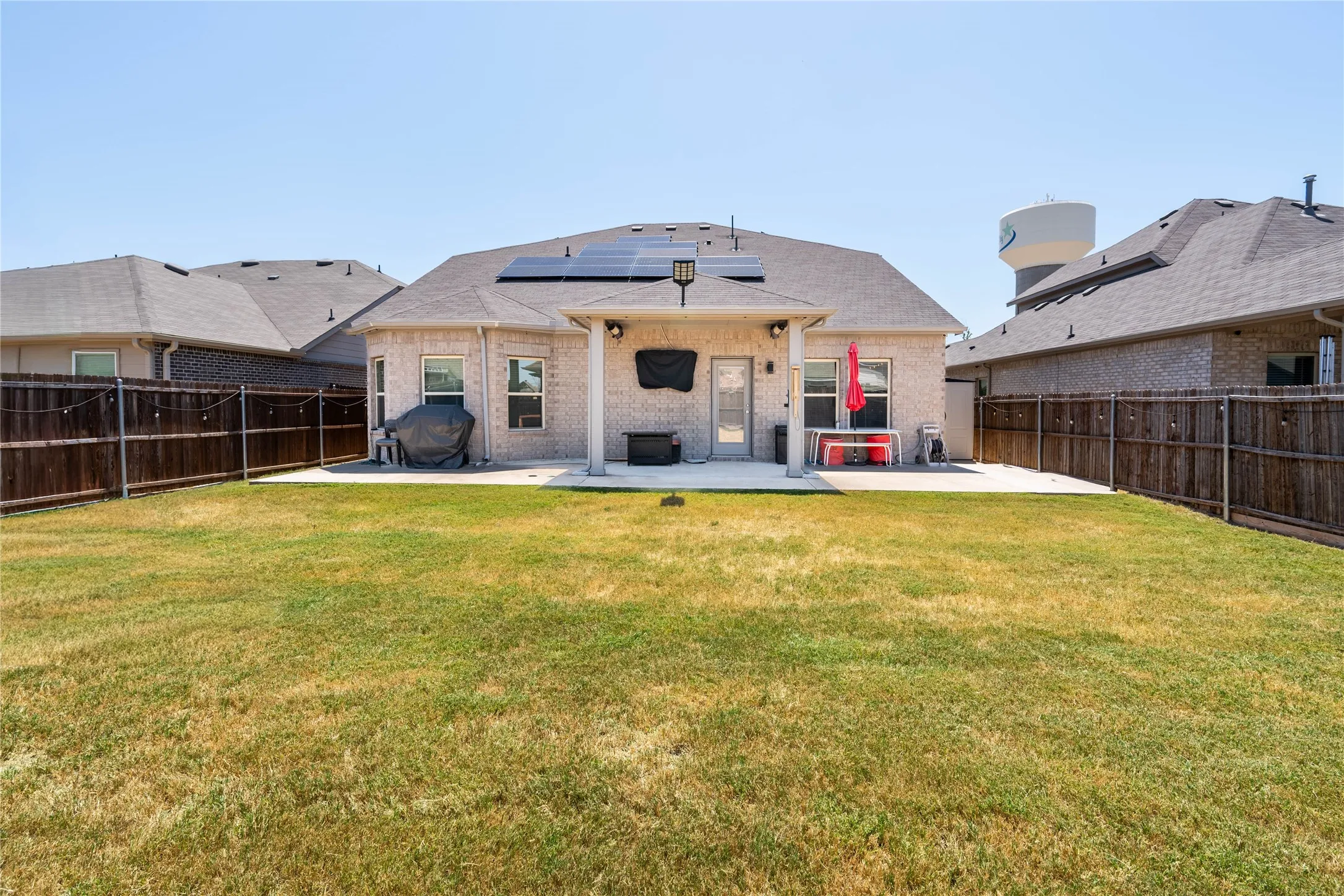 Expansive fenced backyard featuring a covered patio, brick exterior, and solar panels