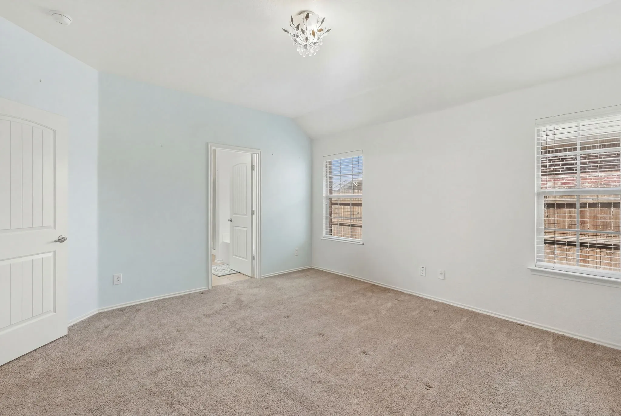 Carpeted flooring, vaulted ceiling, crystal chandelier, two windows with blinds, and a paneled interior door