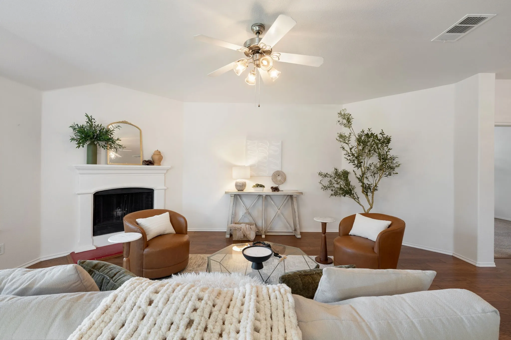 Living area with wood-finish flooring, a white mantel, and a ceiling fan with integrated lighting