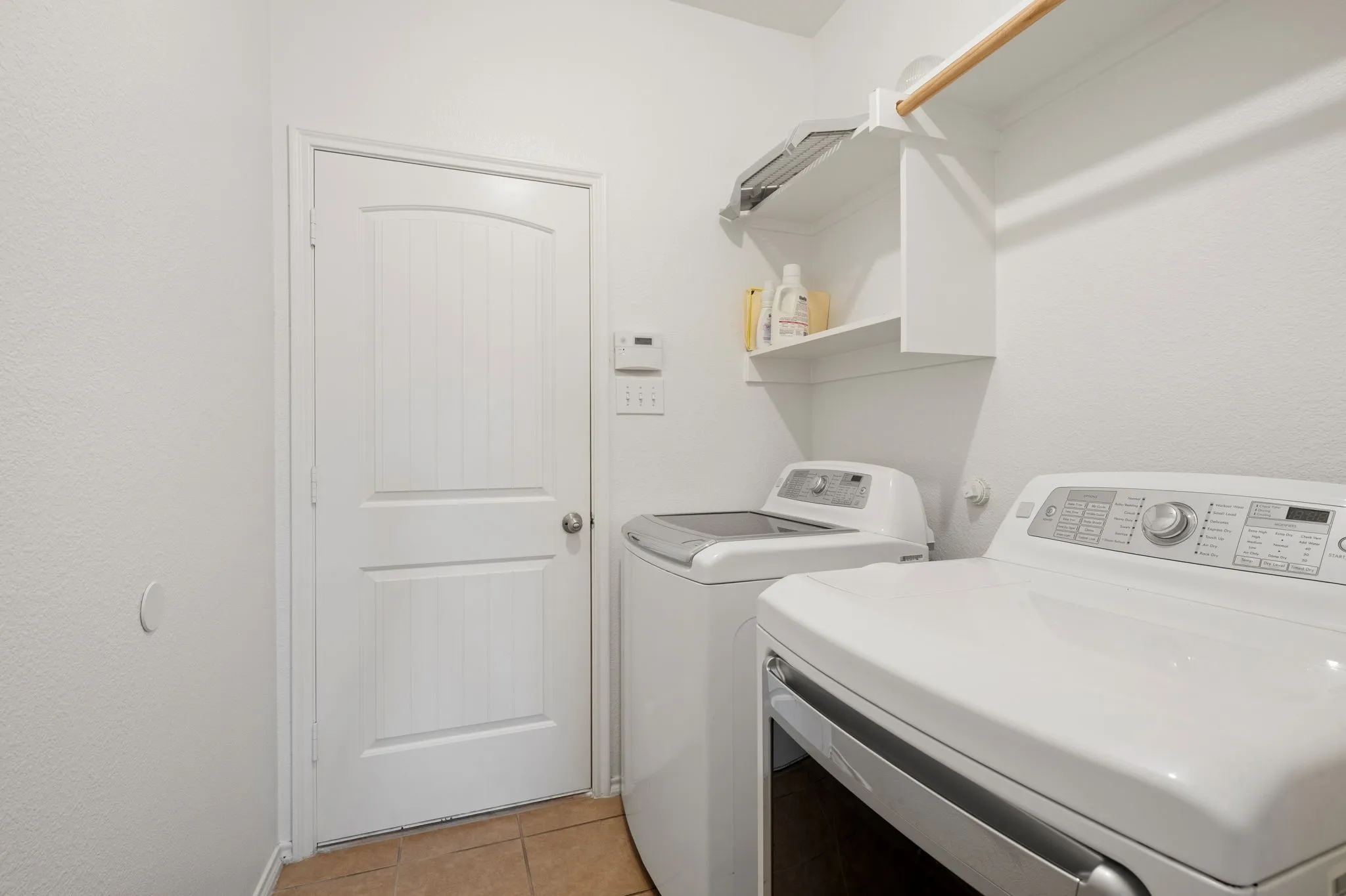 Laundry space featuring tile flooring, white walls, built-in shelving, and a mounted clothing rod