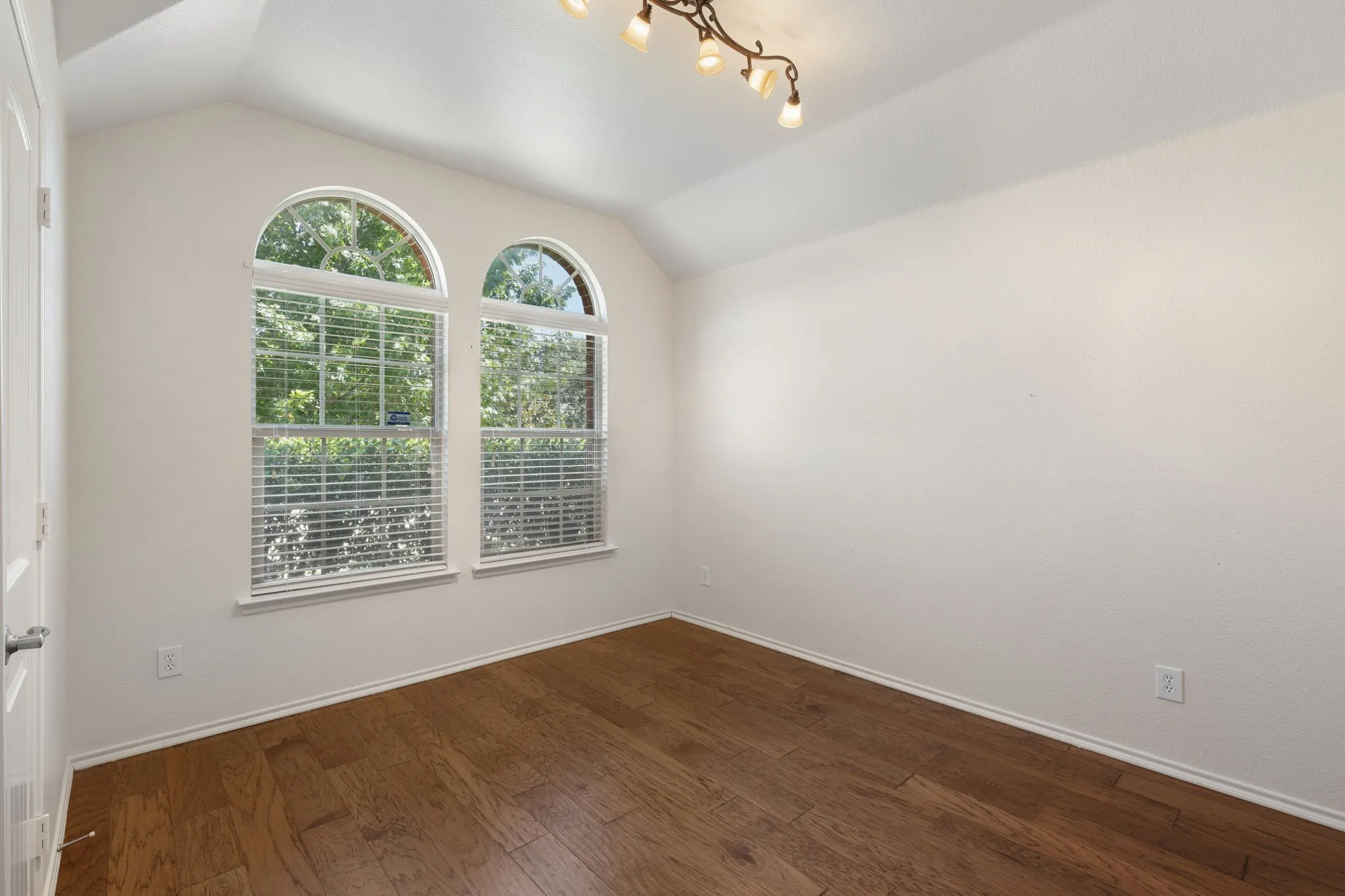 Bedroom with two arched windows, wood-finish flooring, track lighting fixture, and white trim