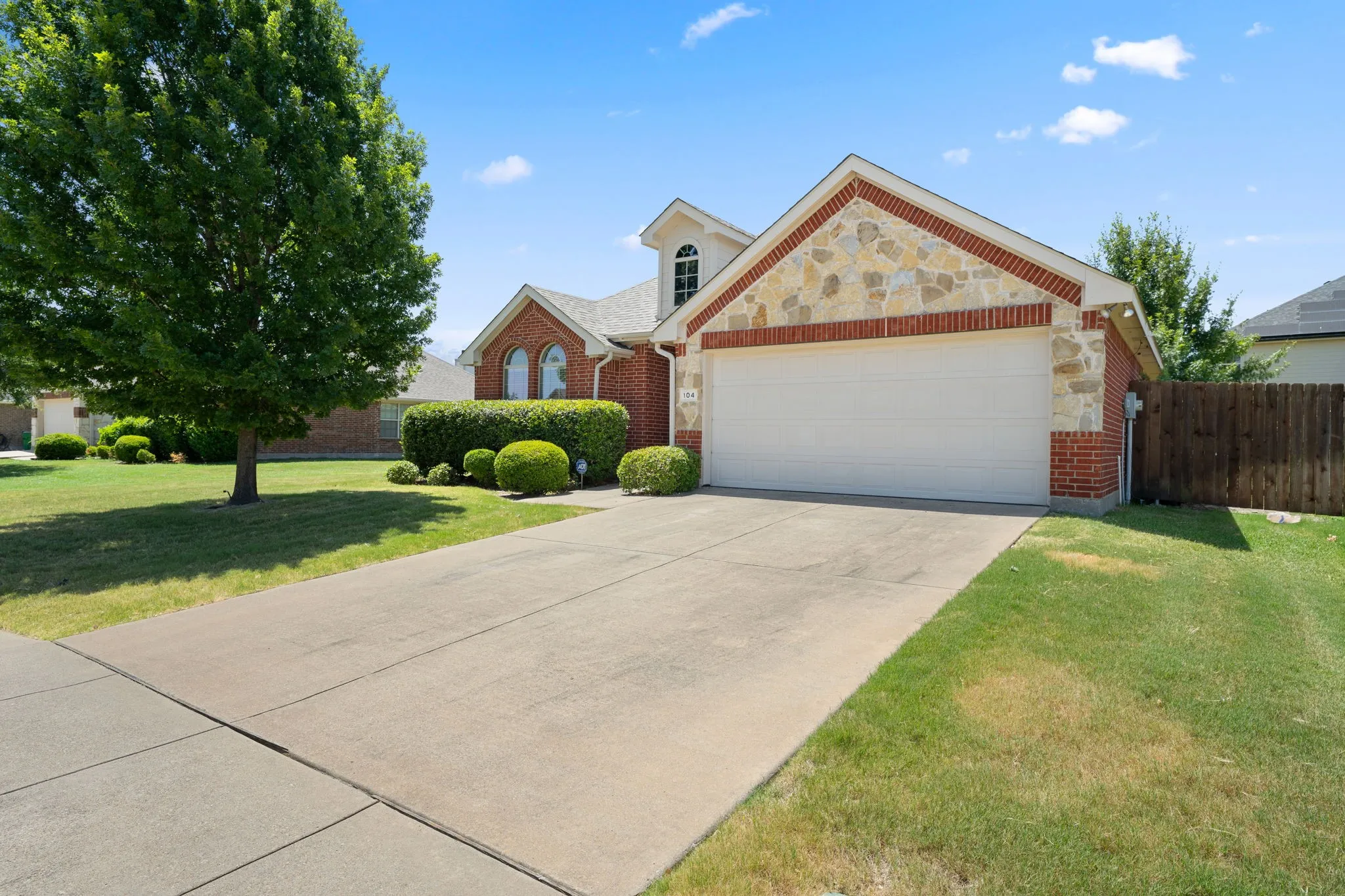 Brick exterior with stone accents, arched windows, attached garage, concrete driveway, and established front landscaping