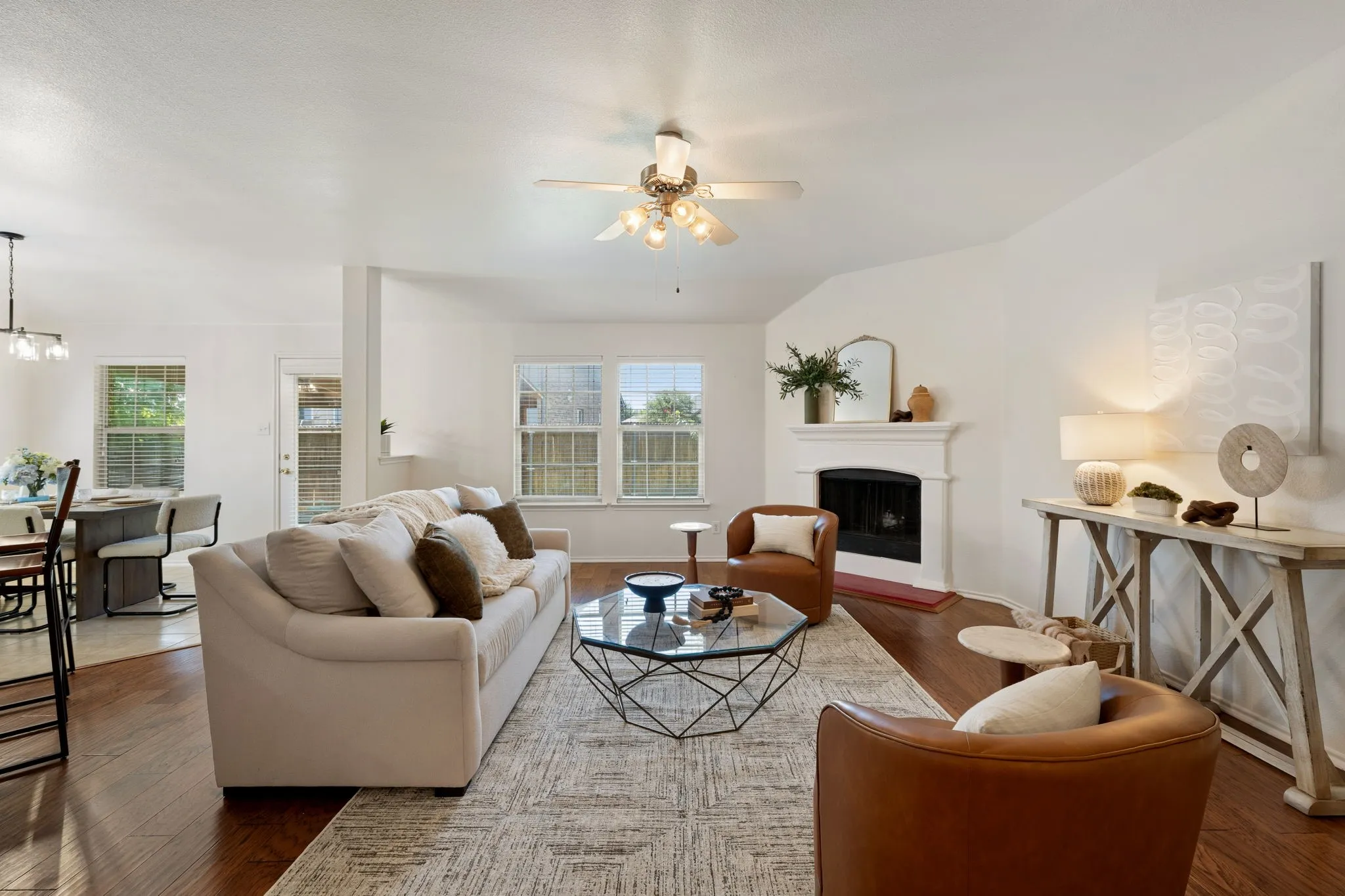 Vaulted living room with a fireplace, wood-finish flooring, and multiple windows