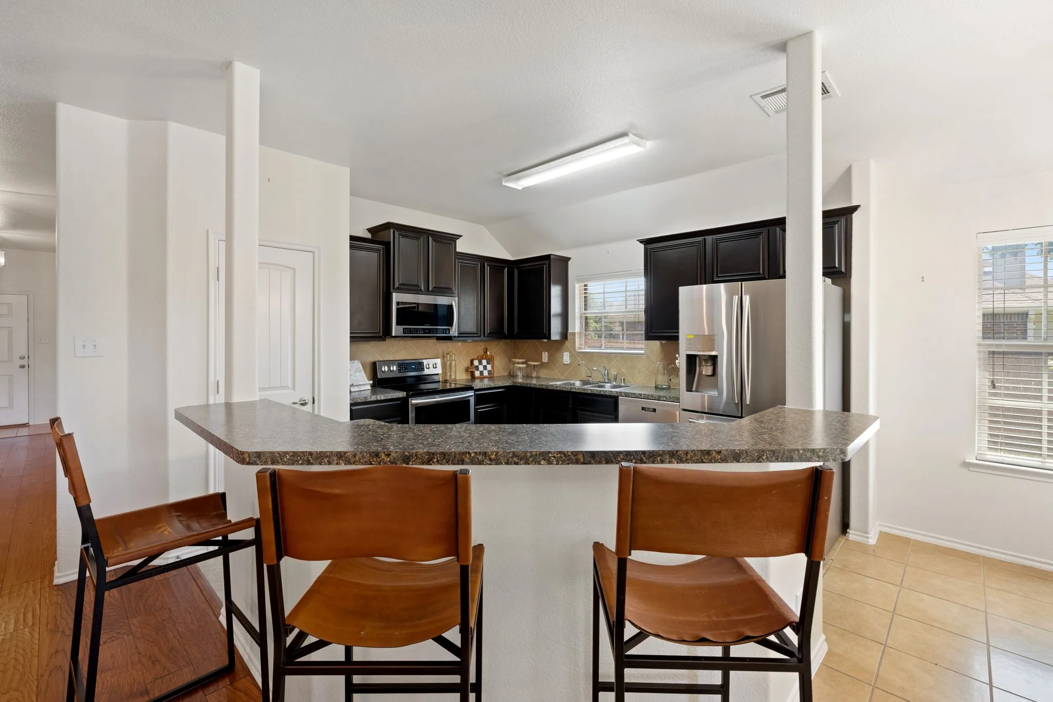 Kitchen featuring dark wood-finish cabinetry, stainless steel appliances, a breakfast bar with a stone-finish countertop, and a tile backsplash