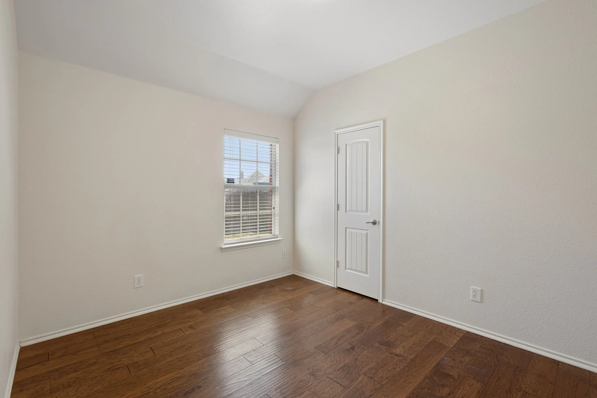Bedroom w wood-finish flooring, white paneled interior door, window with blinds, and light-toned walls