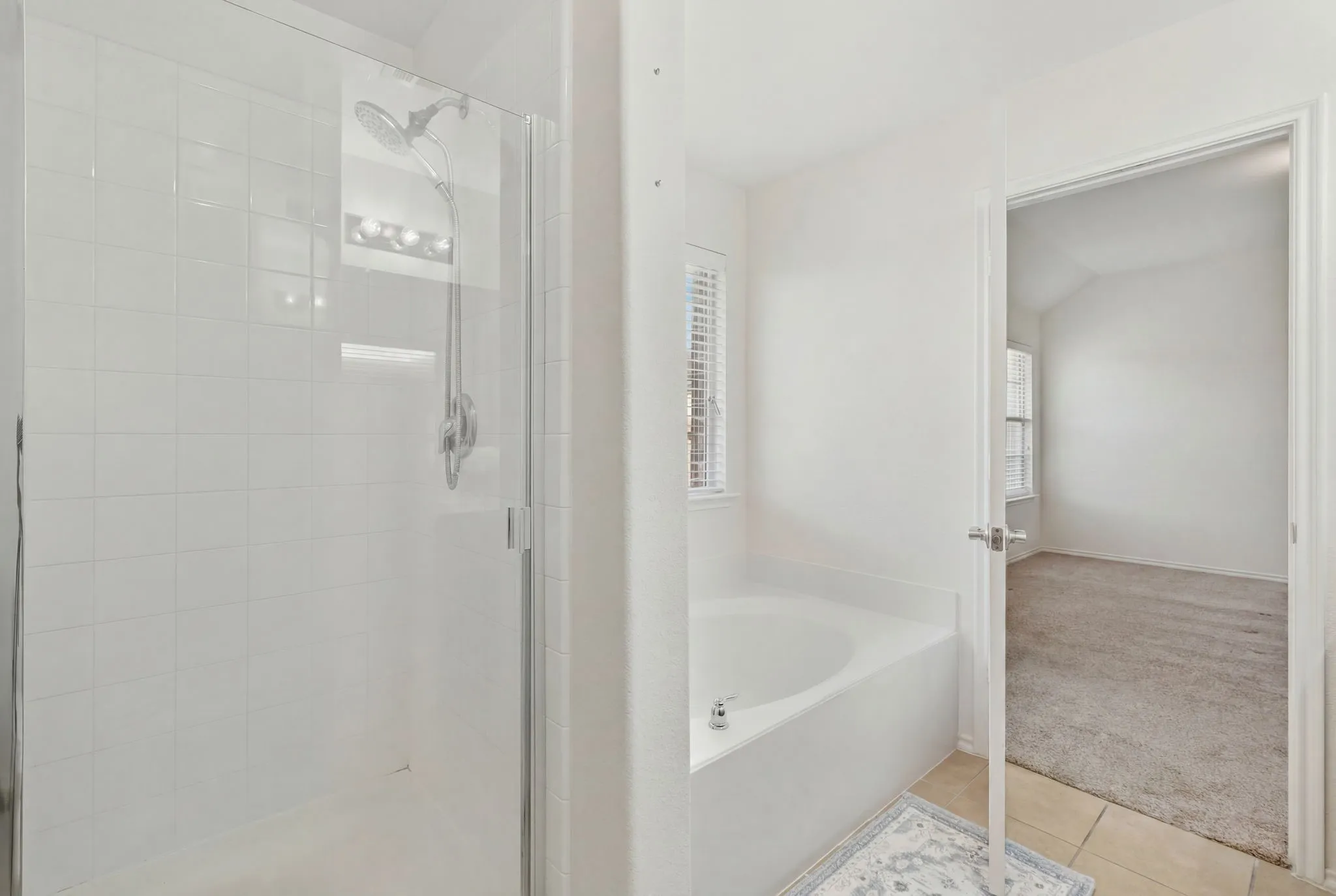 White tiled shower with glass enclosure, separate soaking tub, and tile flooring