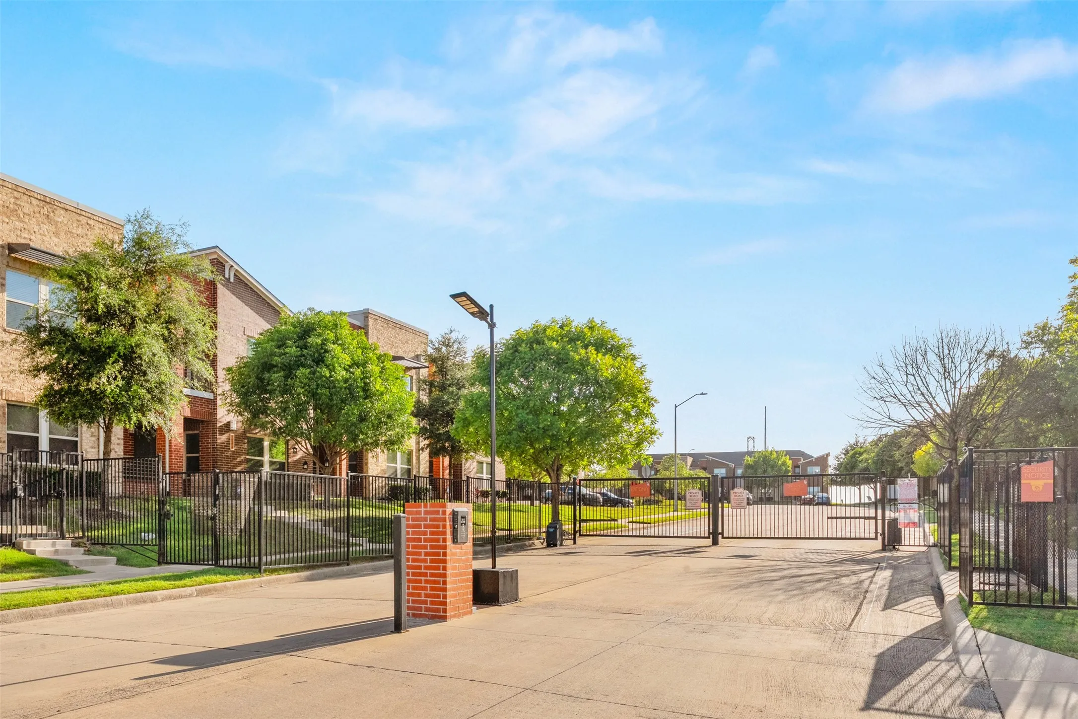 Gated property entrance featuring brick columns, black metal fencing, and mature landscaping