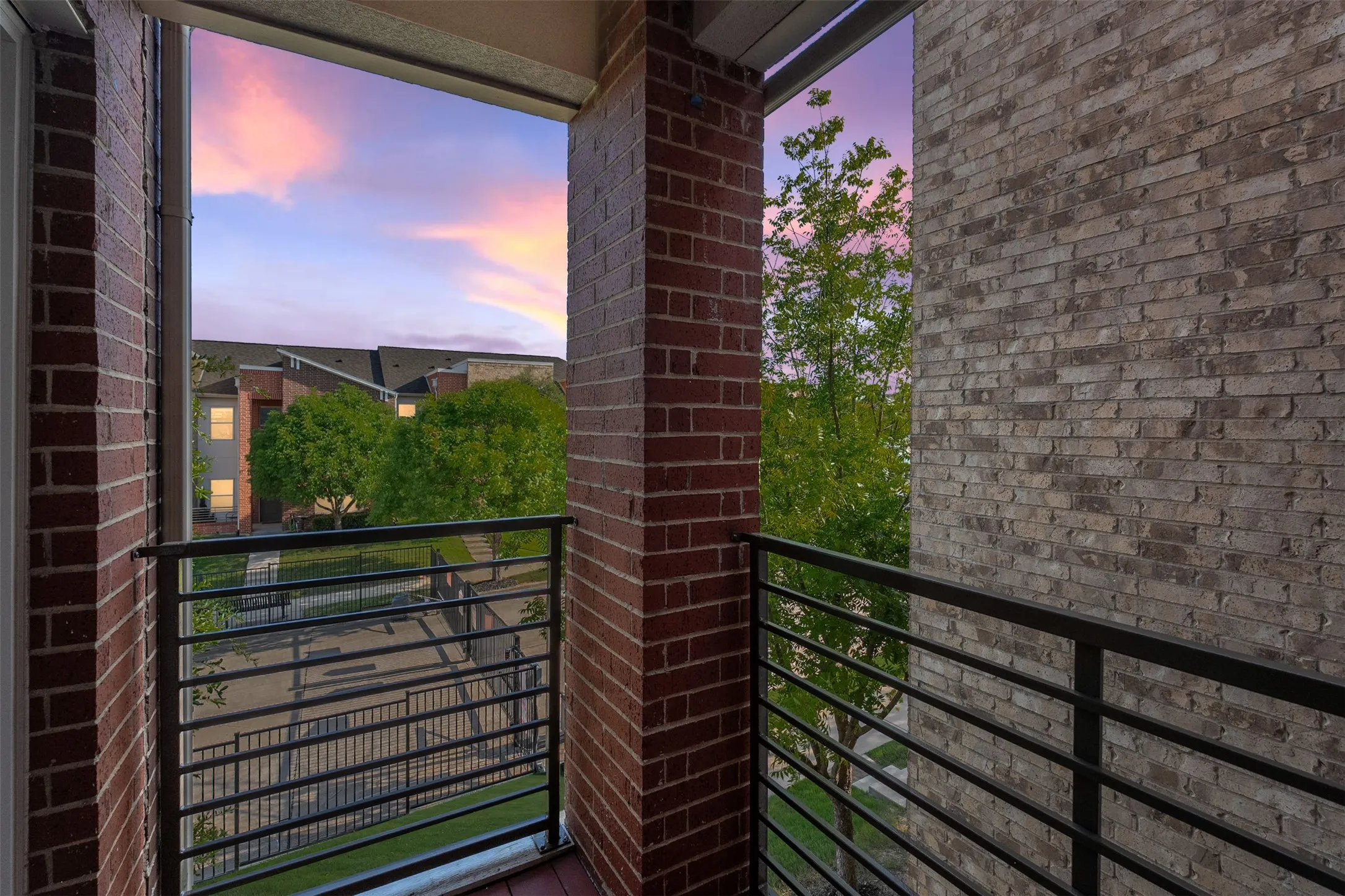 Balcony with brick columns, black metal railing, and wood-finish flooring