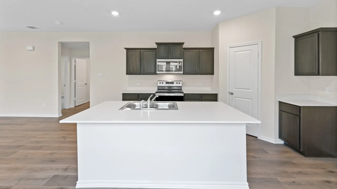 Kitchen featuring an island with an undermount sink, dark wood-finish cabinetry, light countertops, stainless steel appliances, and wood-finish flooring
