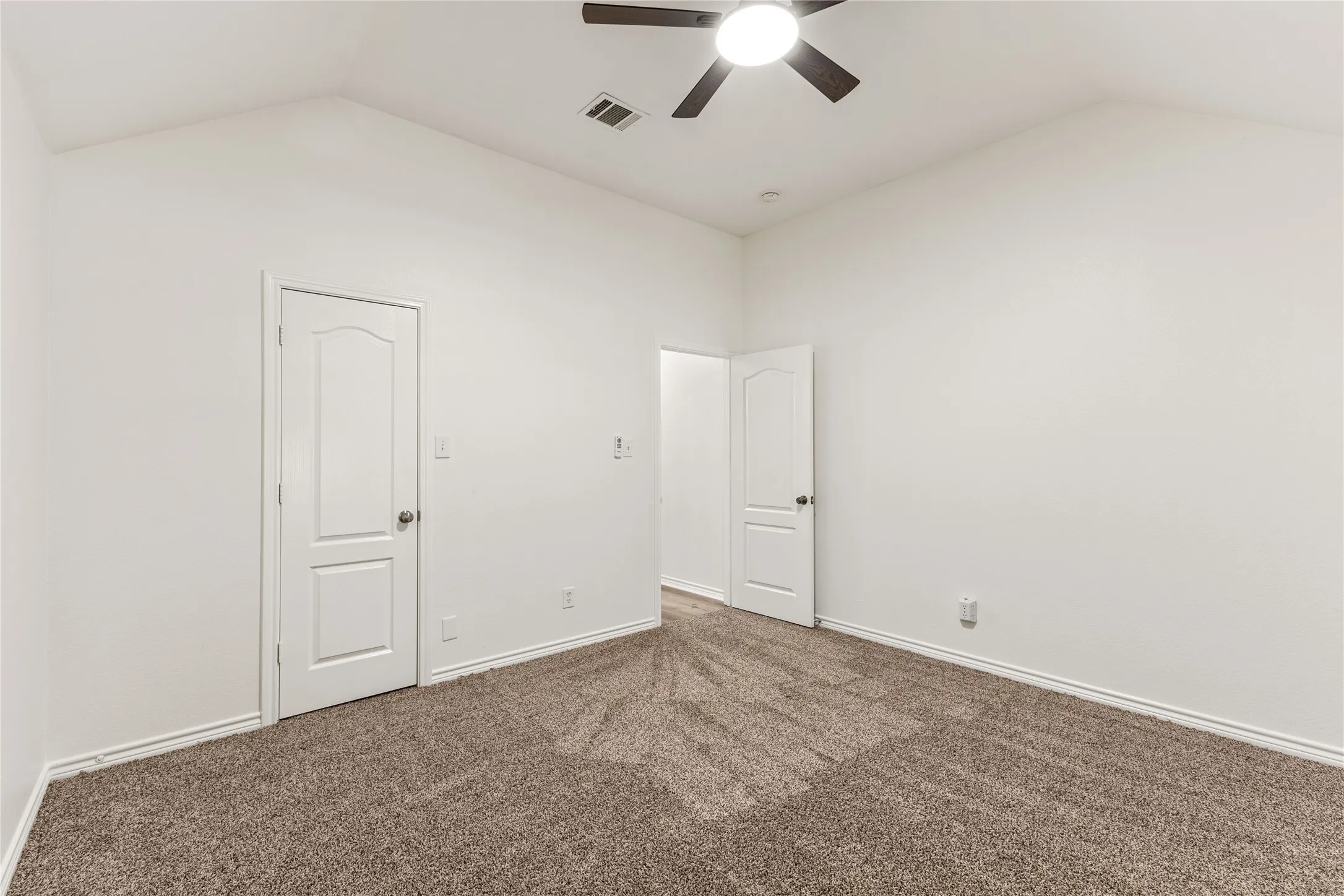 Vaulted ceiling featuring a ceiling fan with integrated lighting, two panel doors, and neutral carpeting