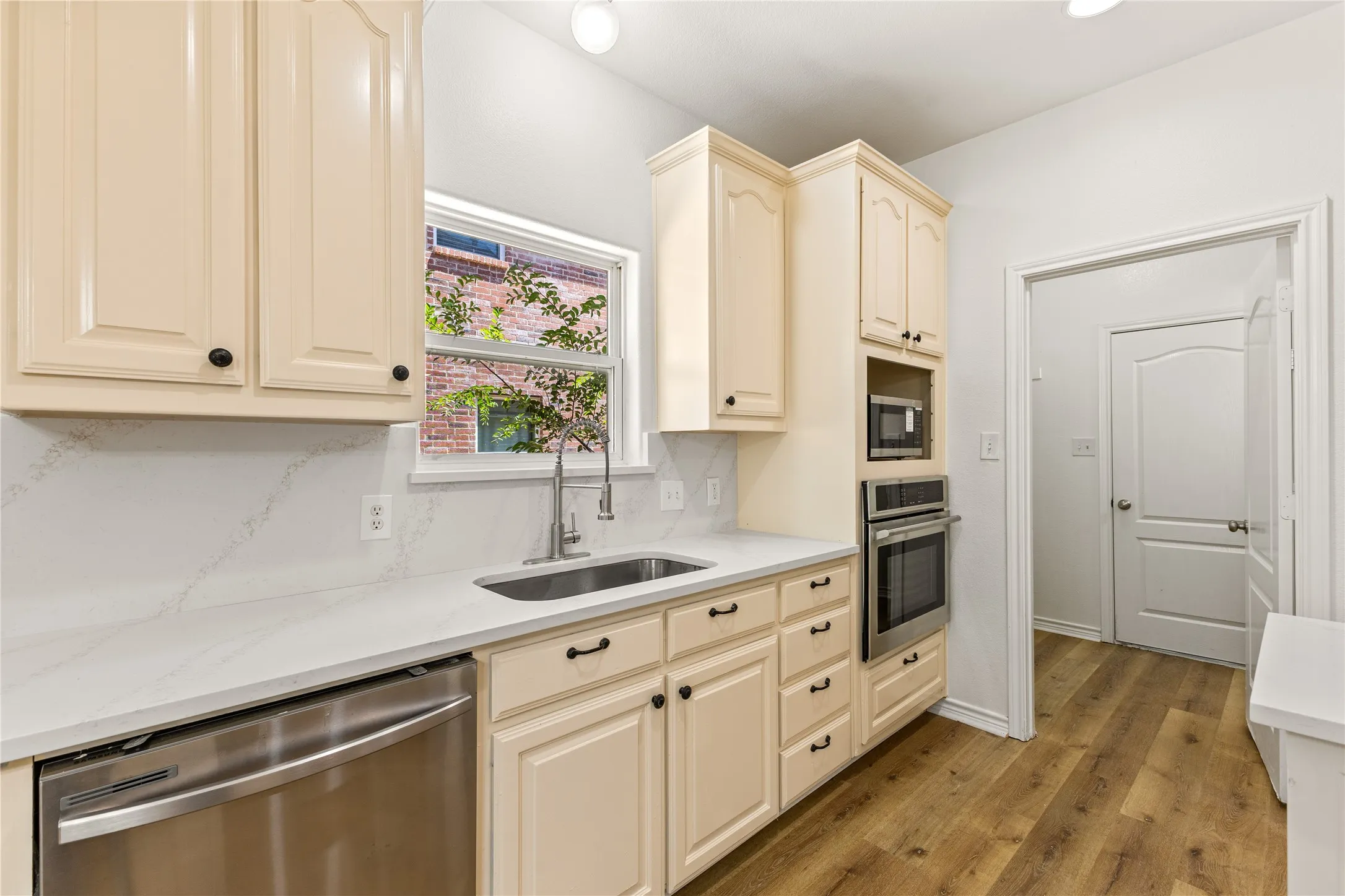 Cream cabinetry, stainless steel sink, built-in microwave, and oven