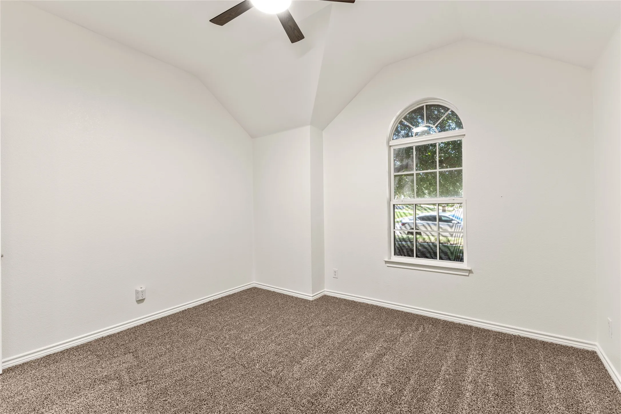 Vaulted ceiling with a ceiling fan, arched window with divided lites, white trim, and neutral carpeting