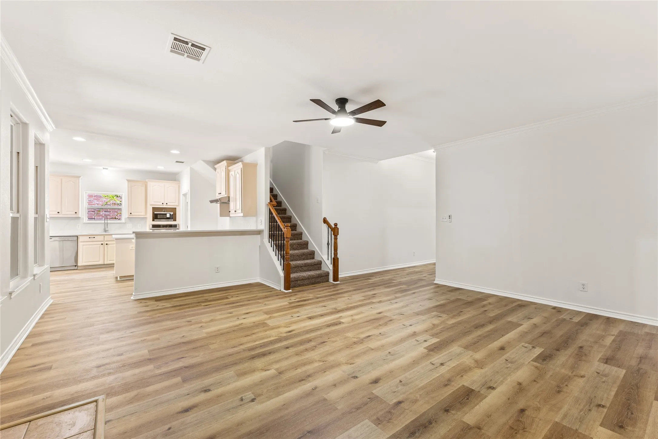 Open-concept living area featuring wood-finish flooring, a ceiling fan, and crown molding